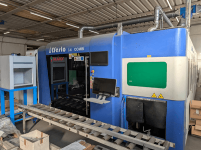 Máquina de corte a laser de fibra EFESTO 3.6 COMBI, vista lateral, com painel de controlo e indicadores de segurança, com exterior azul.