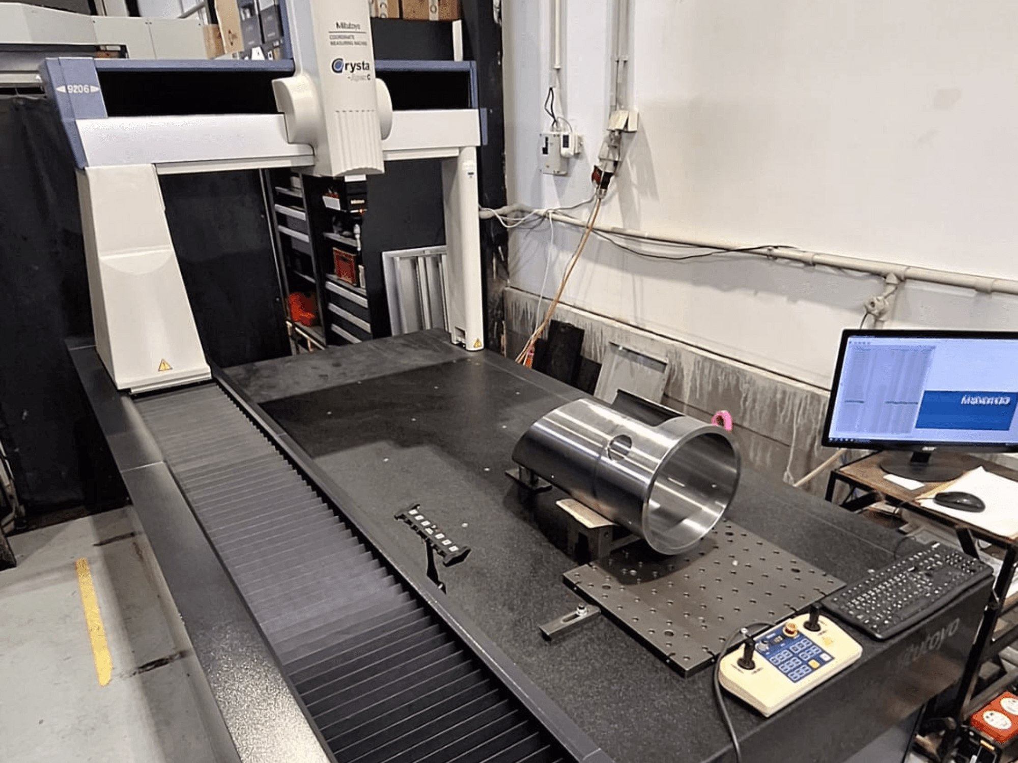 Mitutoyo Crysta-Apex C9206 CMM em vista frontal, medindo uma peça metálica cilíndrica numa placa de superfície de granito preto.