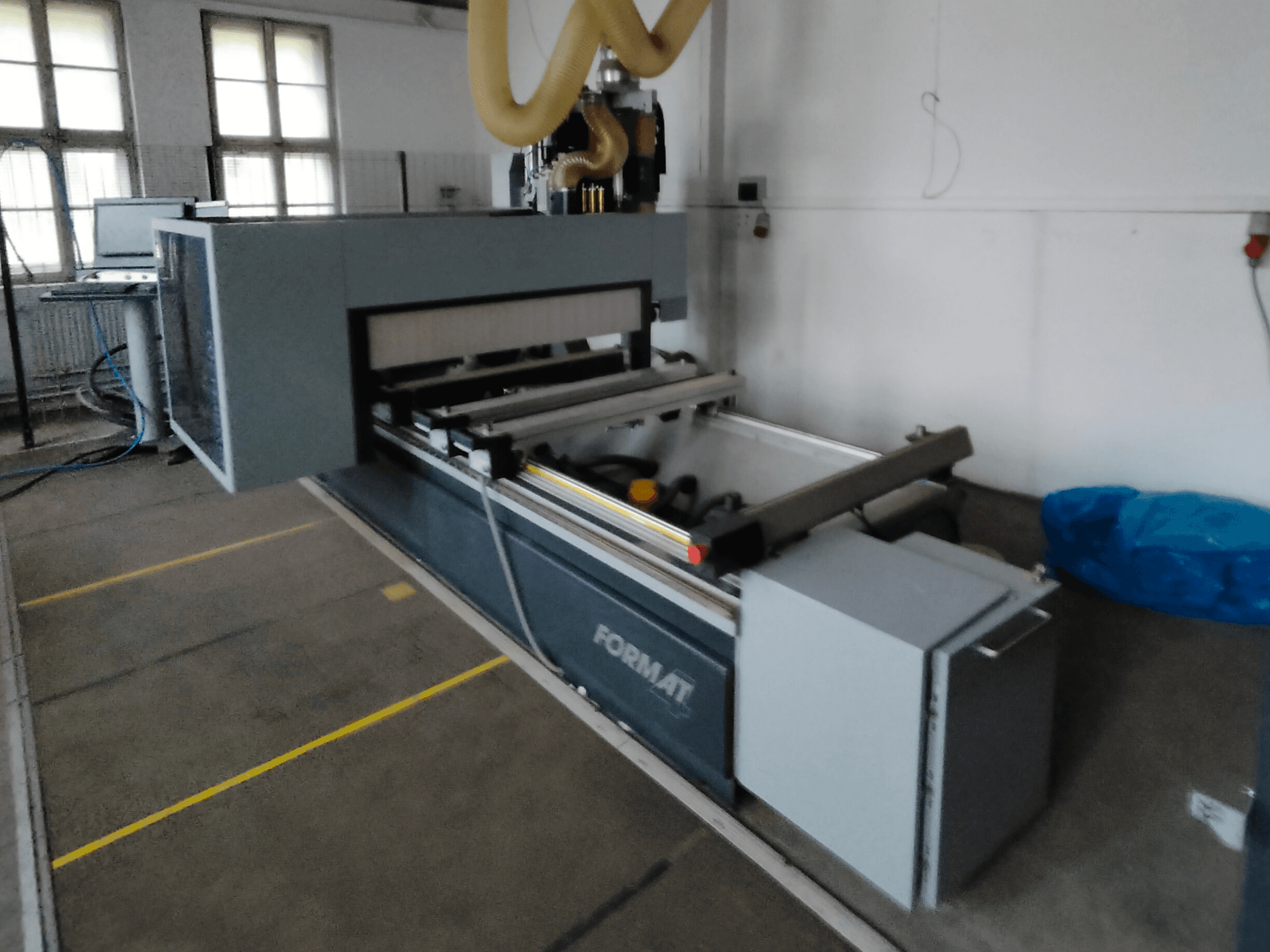 Vista frontal de uma máquina CNC Format com um corpo cinzento, com calhas de guia e um painel de controlo visível.