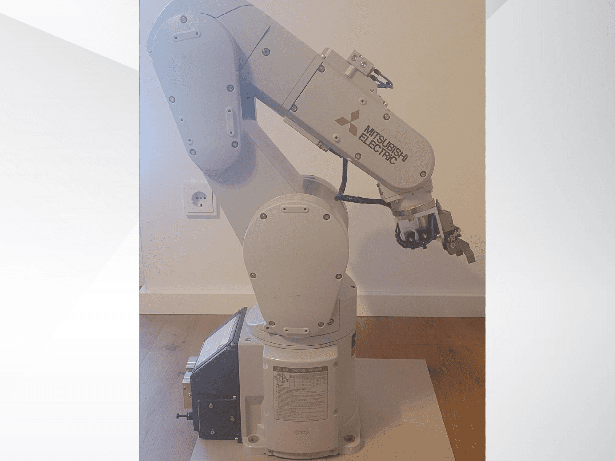Braço robótico da Mitsubishi Electric, vista lateral, com uma pinça e um painel de controlo detalhado na base para definições de funcionamento.