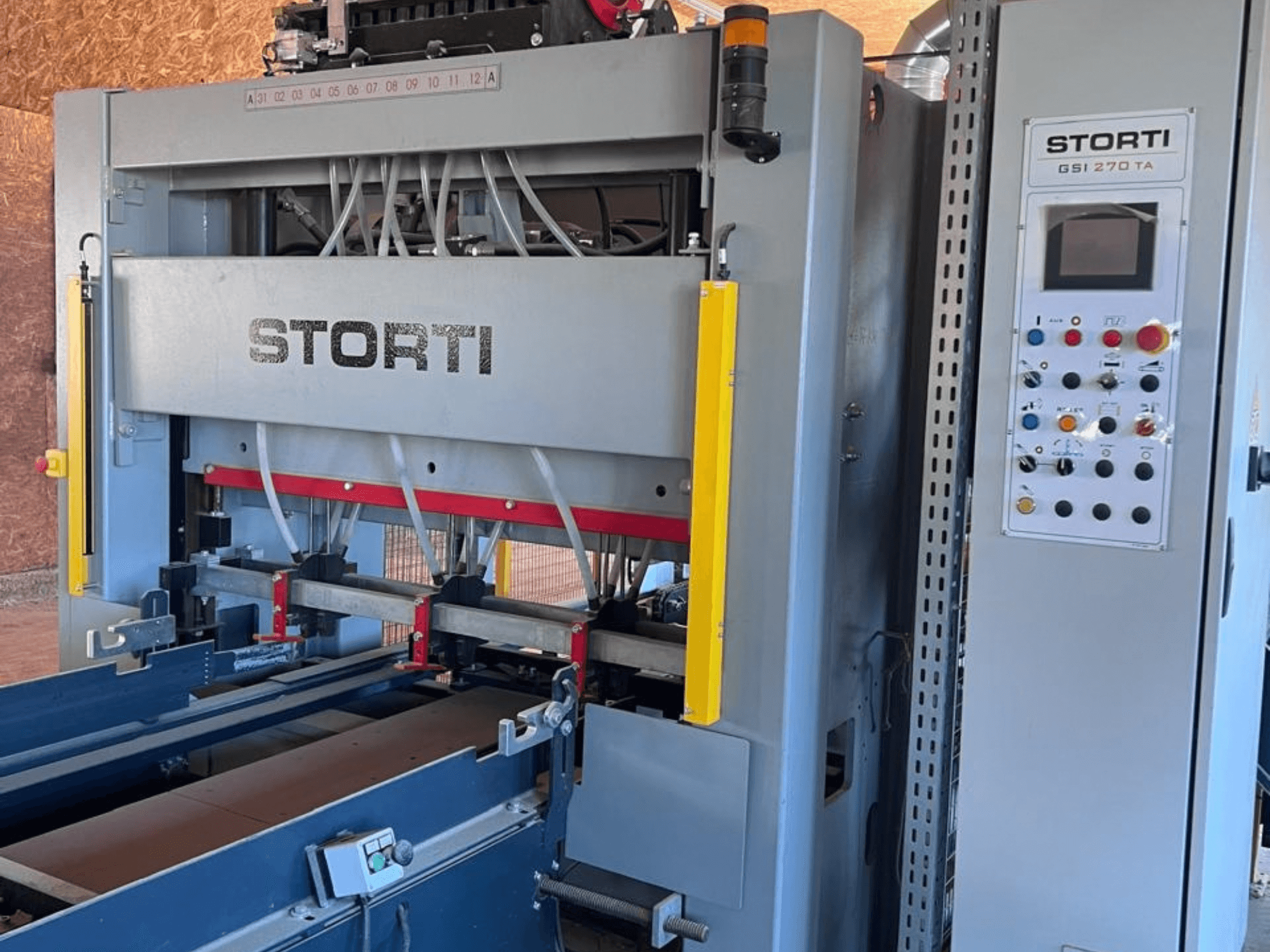 Linha de produção de madeira STORTI GSI 170-270 TA9, vista frontal que mostra o painel de controlo e os mecanismos da prensa hidráulica.