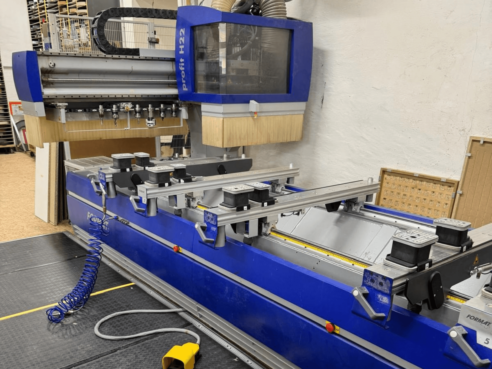 Centro de usinagem de madeira CNC FORMAT4 PROFIT H22, vista frontal, com as ferramentas de usinagem e os grampos de fixação visíveis no corpo azul.