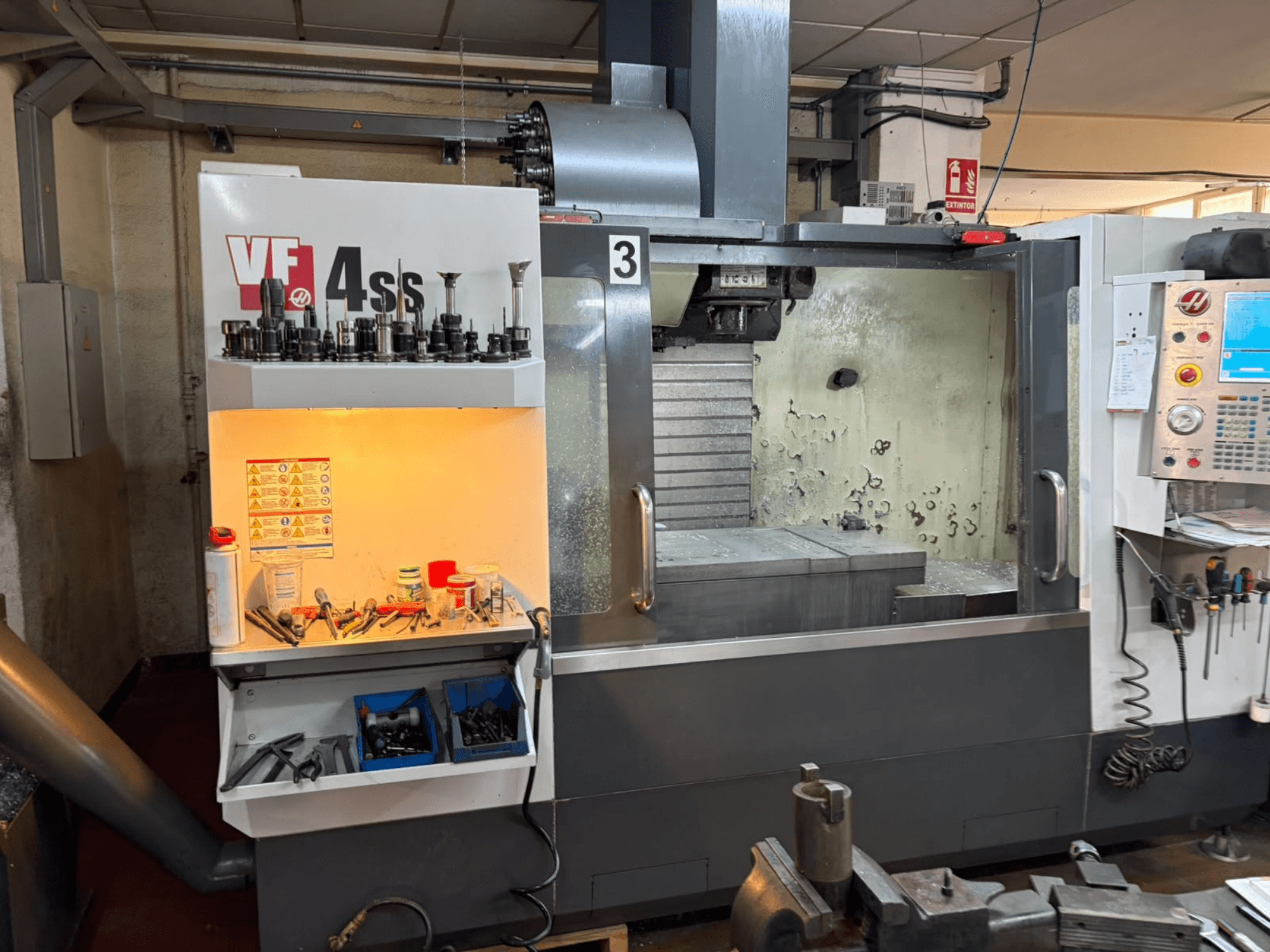 Centro de maquinagem vertical HAAS VP 4SS, vista frontal, com compartimento de armazenamento de ferramentas, painel de controlo e área de trabalho visível, com detalhes da maquinagem.