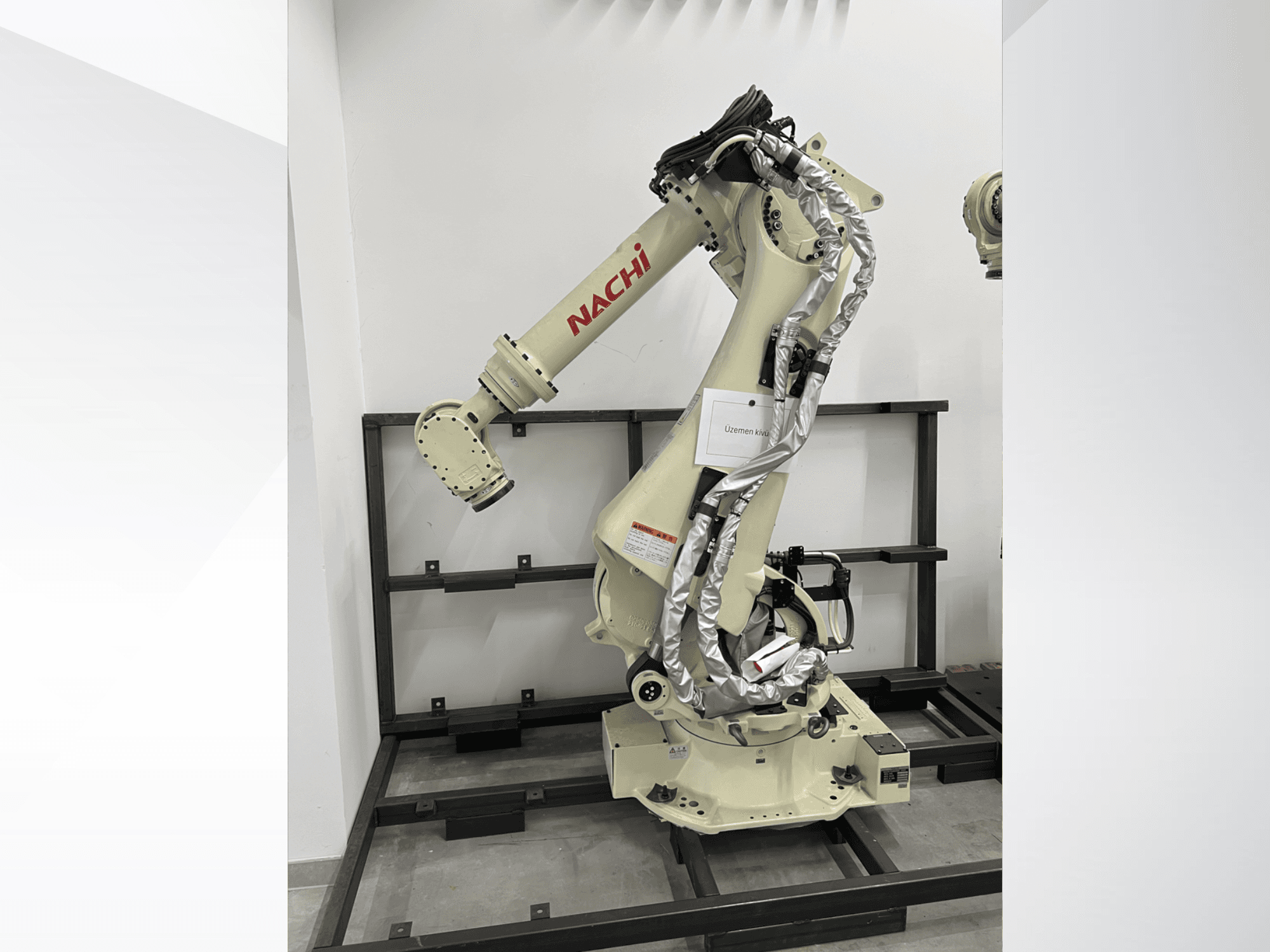 Braço de robô NACHI SRA166-01 em vista lateral, com articulações flexíveis, cabos ligados e montado numa estrutura de proteção.