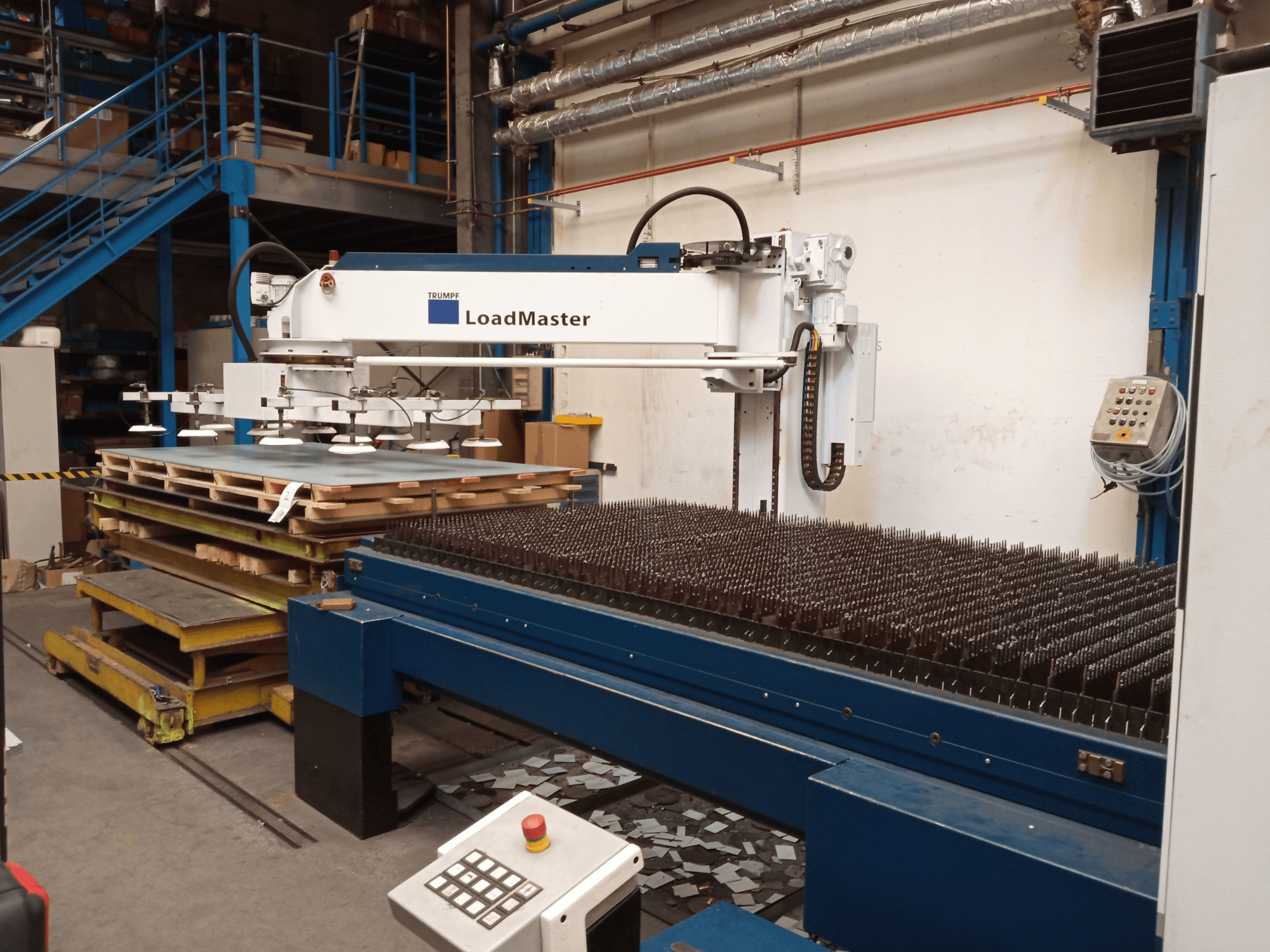 Máquina de corte a laser de CO₂ TRUMPF TruLaser 3030, vista de perfil, equipada com um LoadMaster e paletes de materiais.