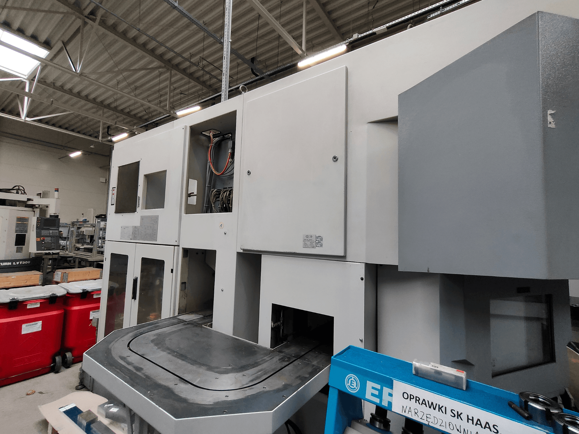 Virador vertical EMAG VSC 250 mostrado de lado, com painéis de controlo e uma grande área de trabalho.