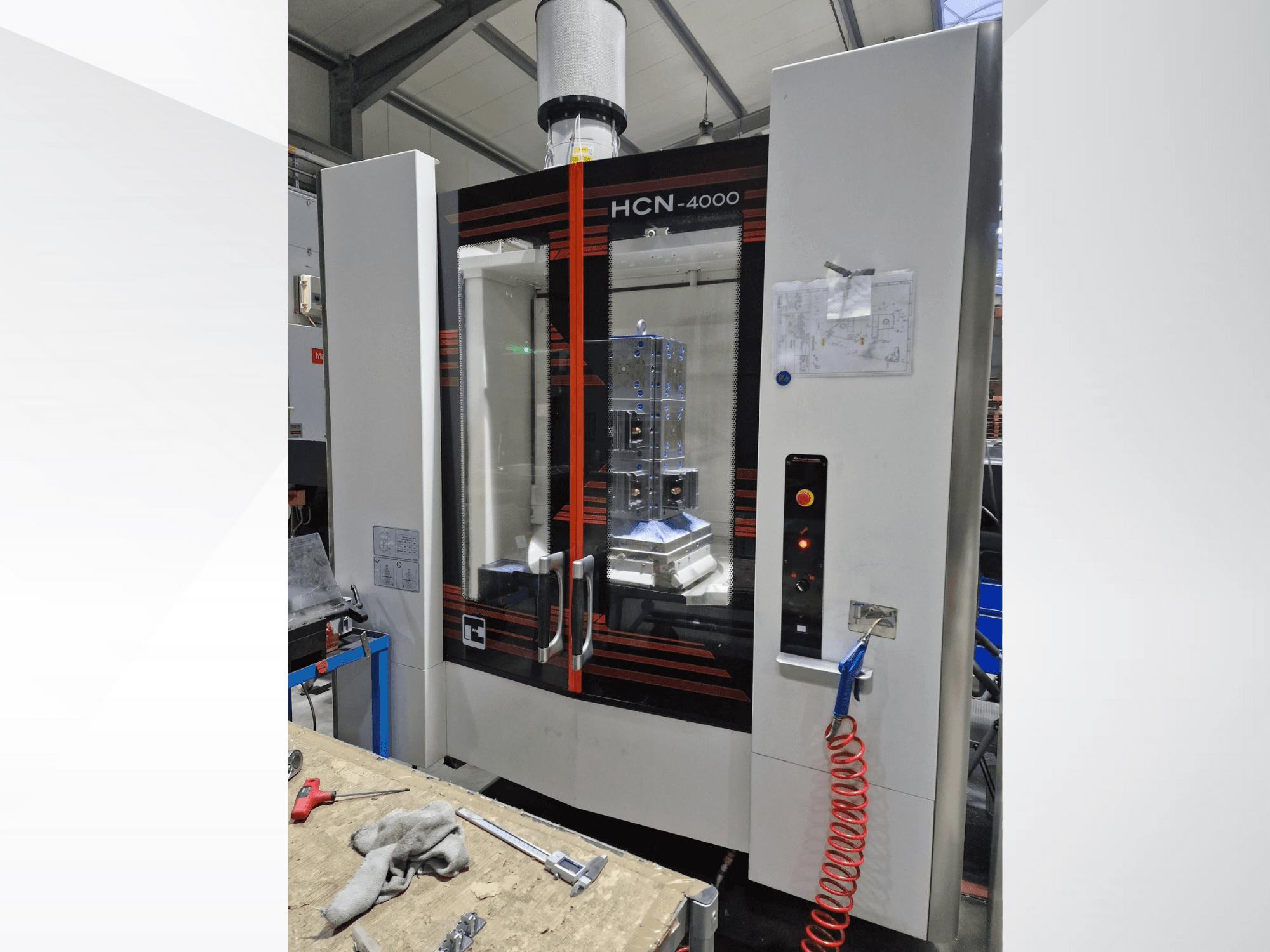 Máquina CNC HCN-4000 em vista frontal, com um painel de vidro, painel de controlo com botões e uma planta anexada.