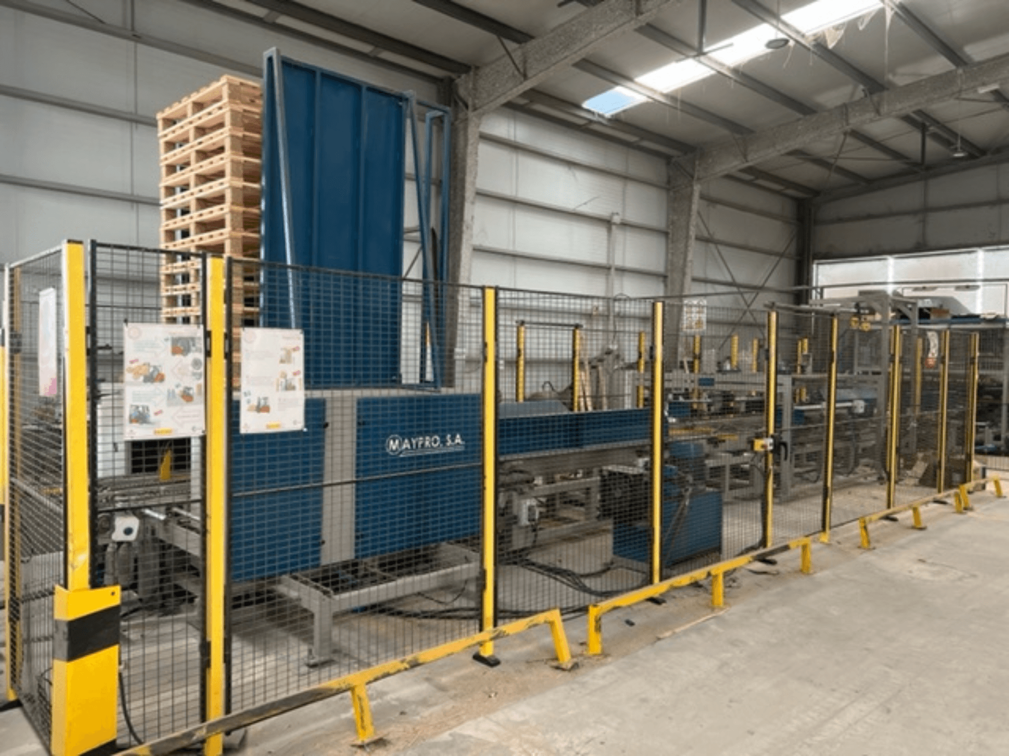Máquina industrial de embalagem de paletes da Maypro S.A. num armazém, com rede de segurança e controlos operacionais, vista lateral.