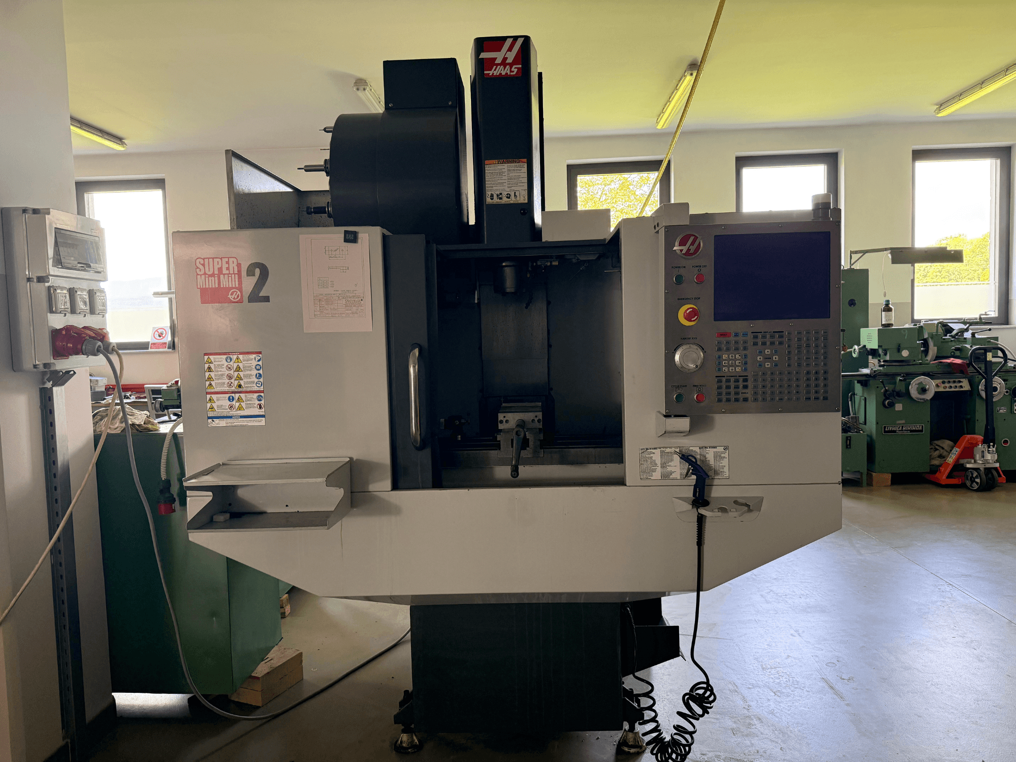 Centro de maquinação vertical Haas Mini Mill 2 em vista frontal, mostrando o painel de controlo e a área de ferramentas com etiquetas de aviso.