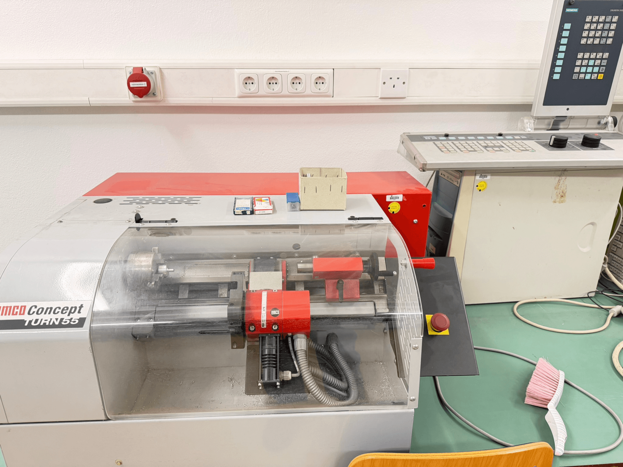 Máquina de tornear horizontal EMCO Concept Turn 55 com exterior vermelho e cinzento, vista frontal mostrando os controlos e a área de trabalho.