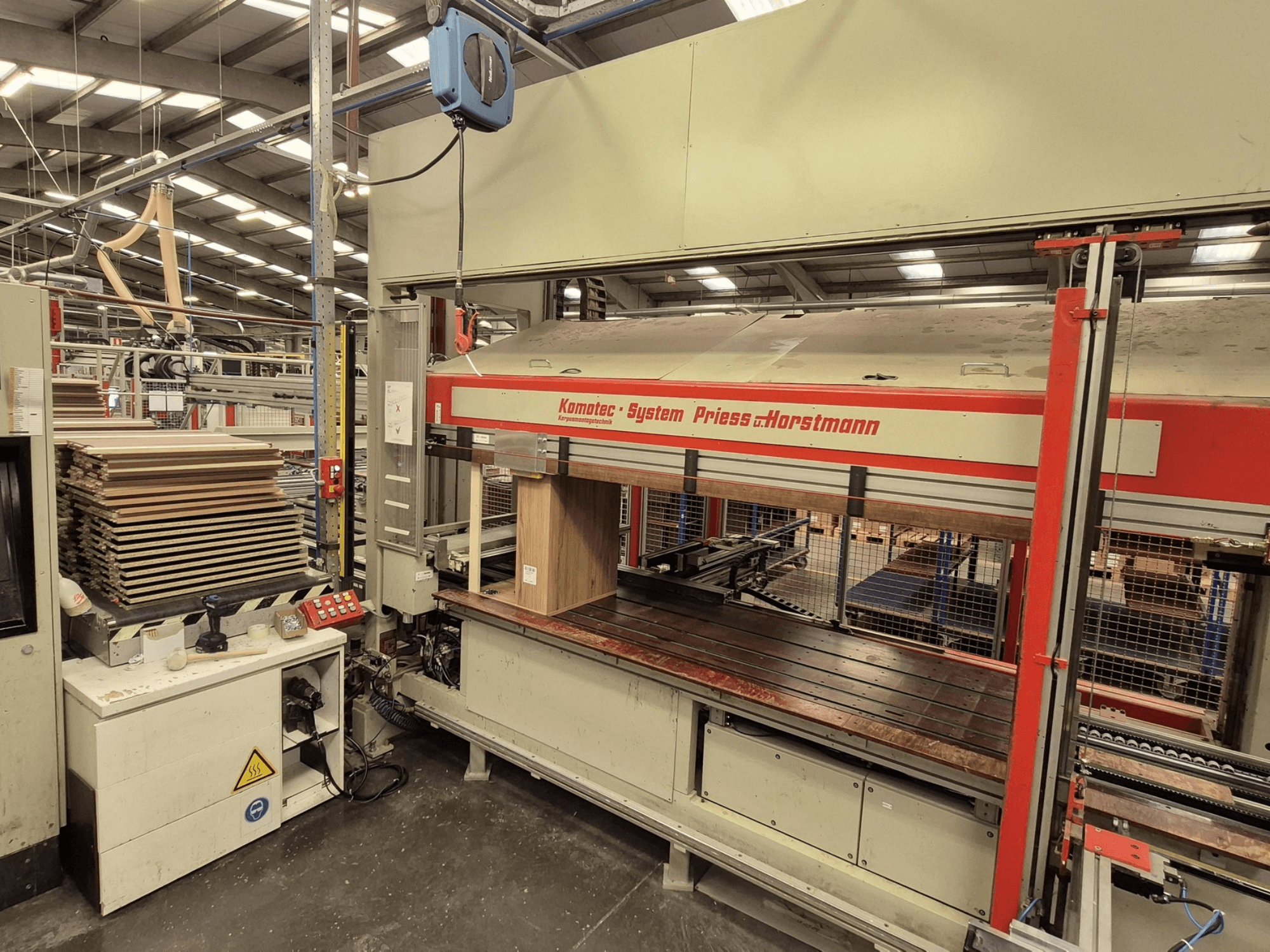 Prensa de folheado KP-5-CNC da PREISS U HORTSTMANN, vista frontal, mostrando folhas de folheado empilhadas e painel de controlo.