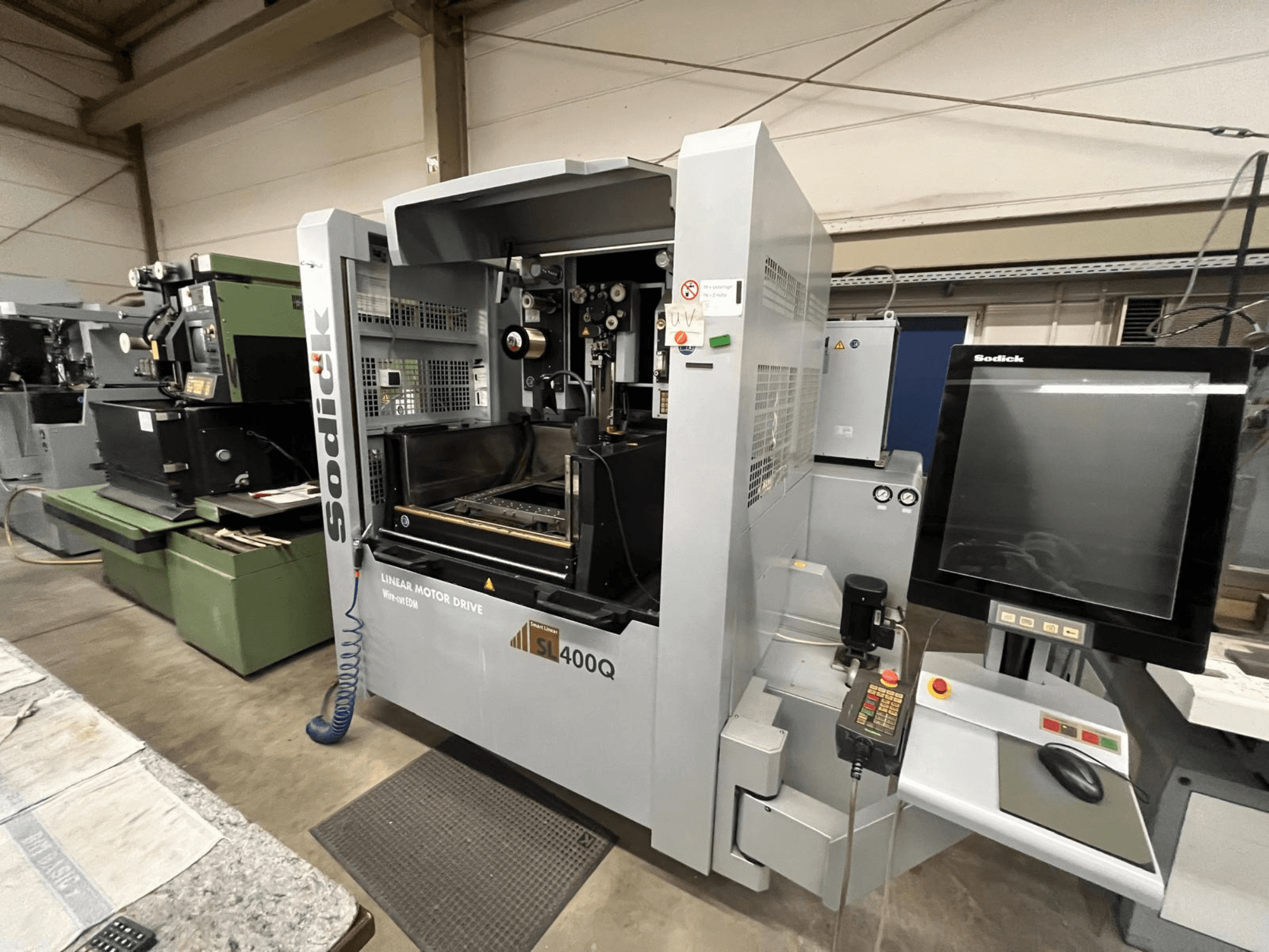 Máquina CNC com motor linear Sodick SL400Q, vista frontal com painel de controlo digital e visor numa oficina.