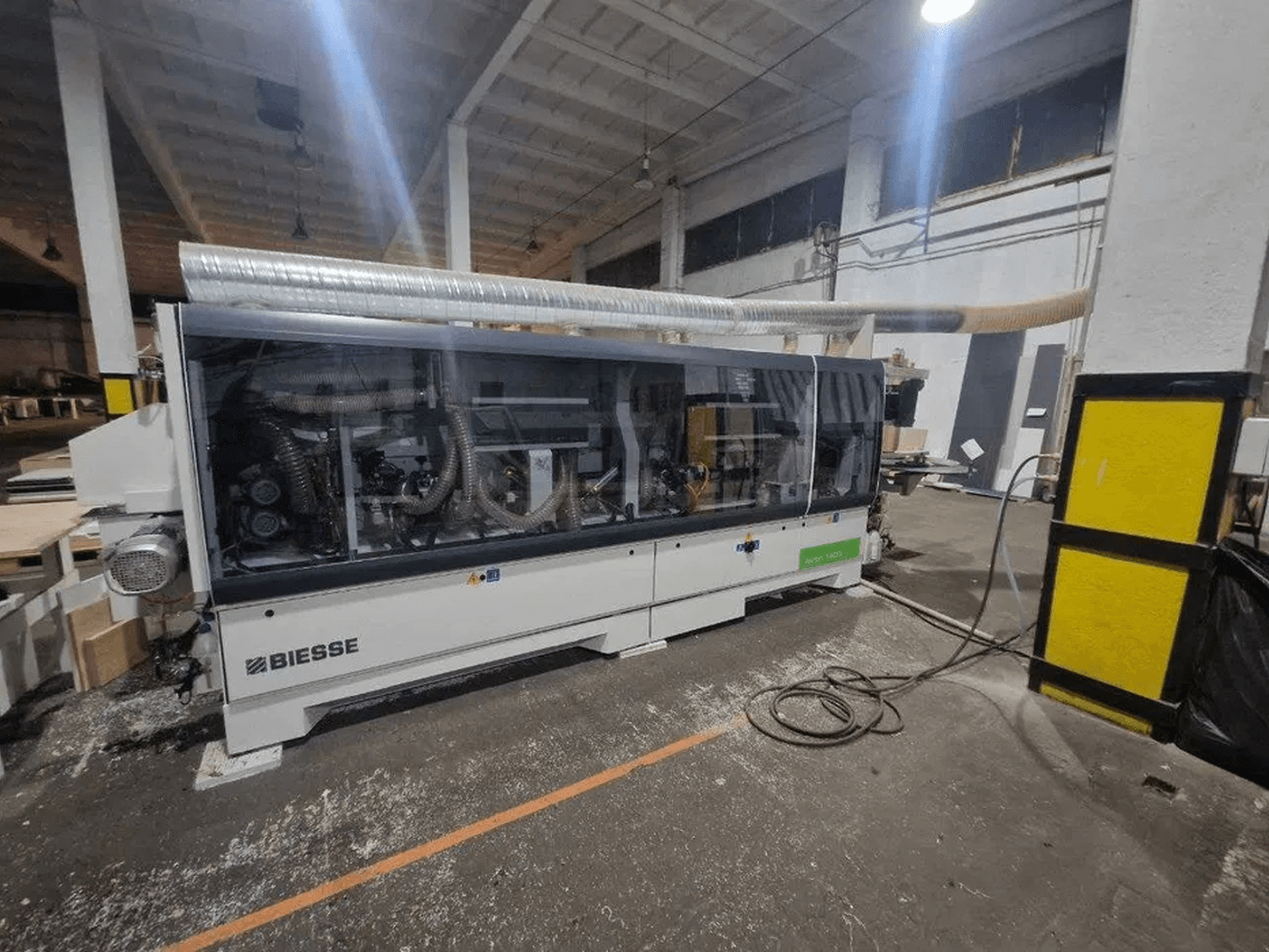 Uma encoladora de bordas BIESSE Akron 1440 A numa oficina, com uma cobertura transparente e componentes da máquina visíveis.