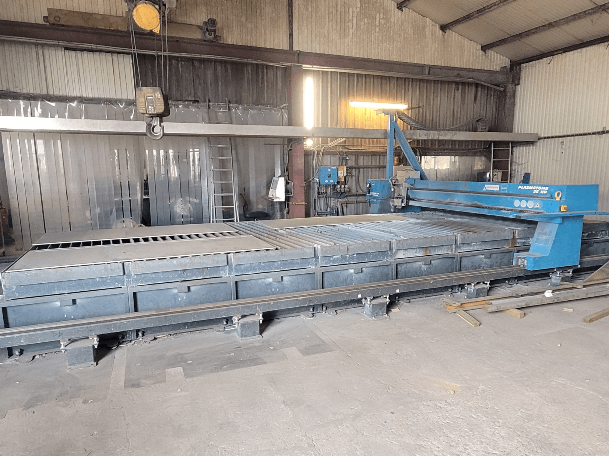 Máquina de corte plasma SAF Plasmatone 25Hp, vista lateral, mostrando a base de corte e os componentes operacionais num ambiente industrial.