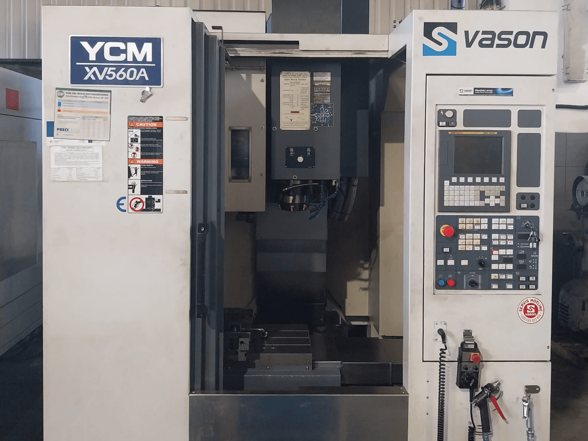 Vista frontal do Centro de Maquinação Vertical YCM XV 560A, com painel de controlo e mesa de trabalho com componentes de maquinação visíveis.