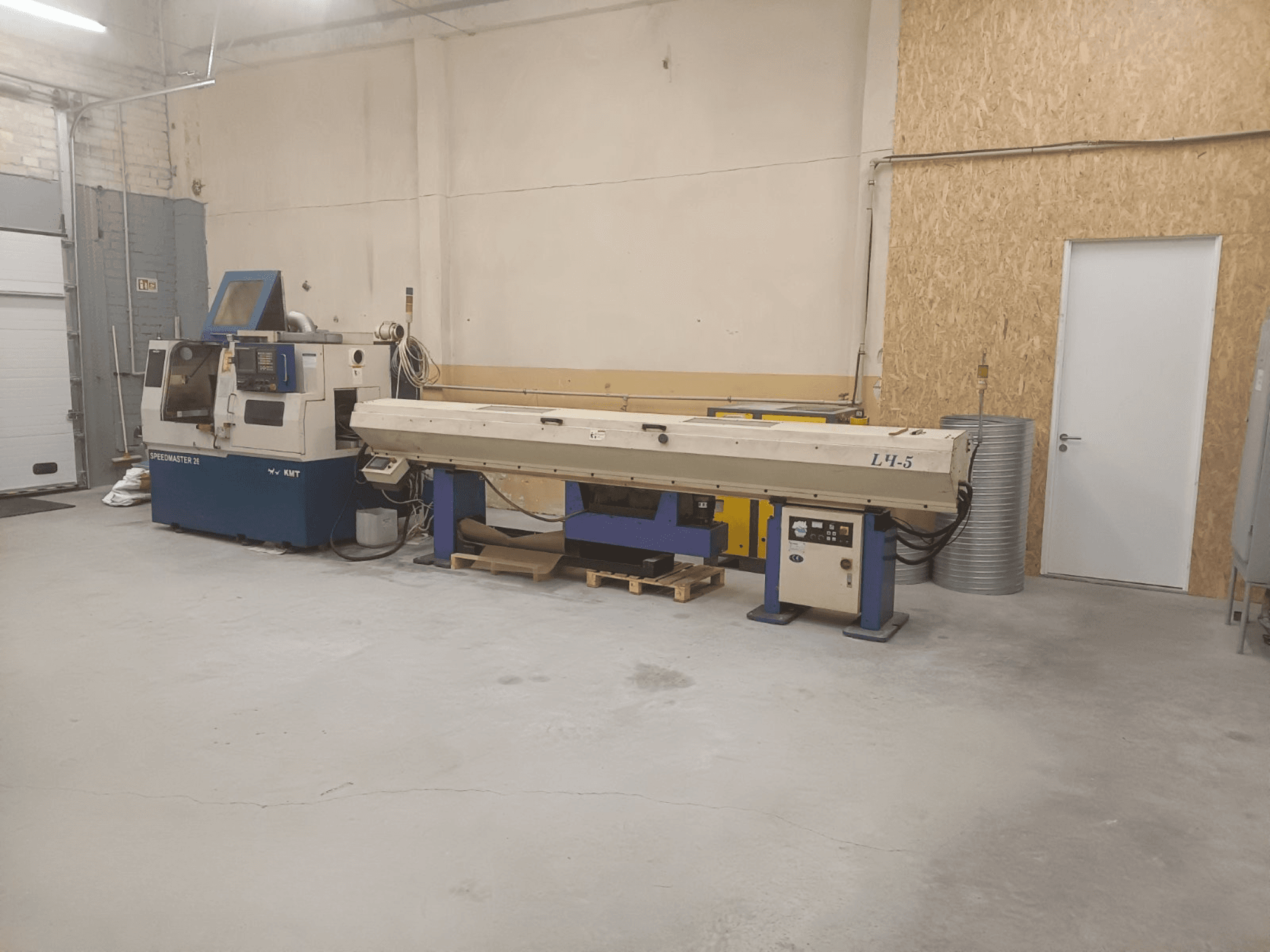 Oficina industrial com a máquina KMT Speedmaster 34 e a L4.5, vista de frente, com controlos e máquinas visíveis.