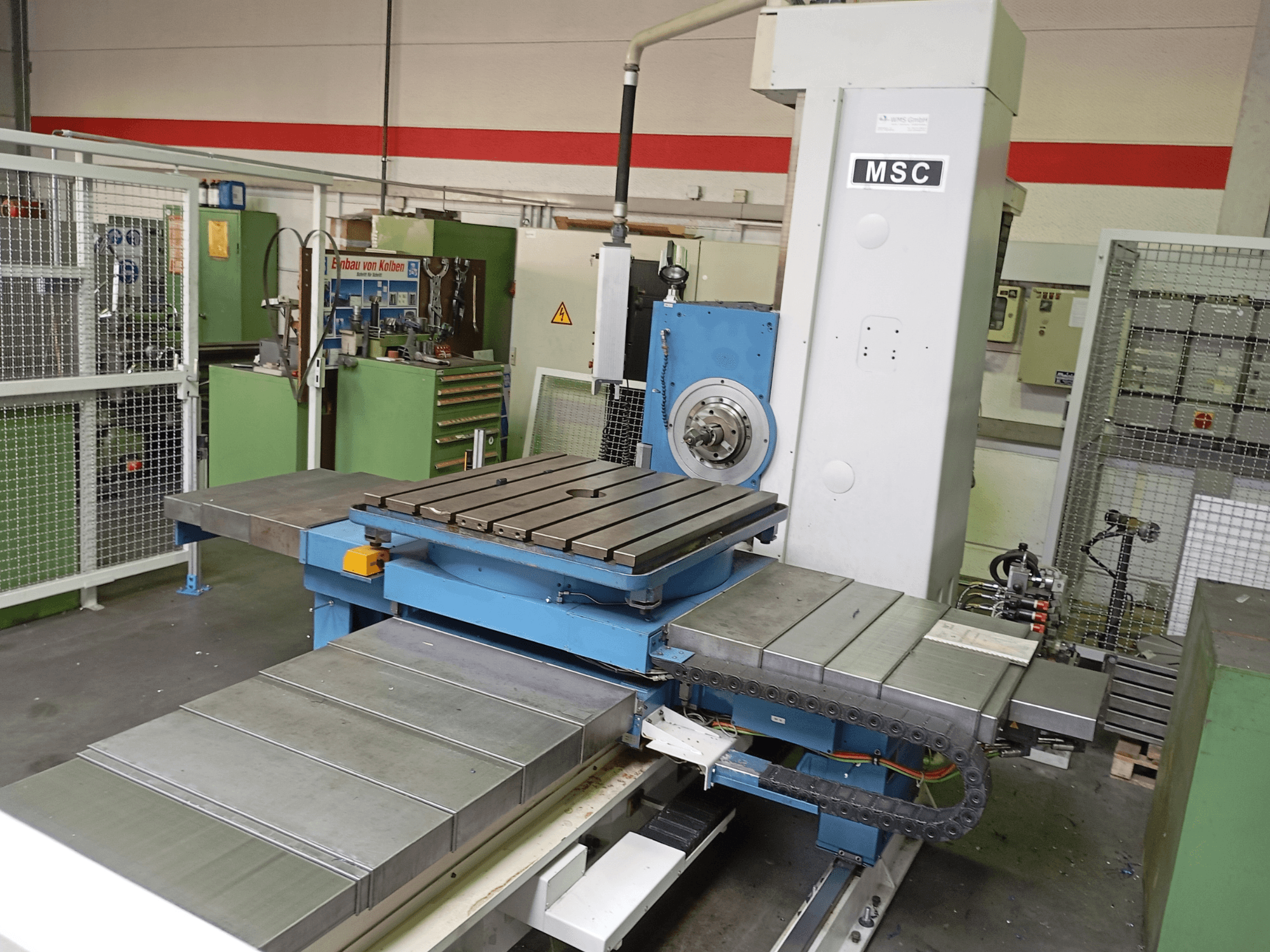 A máquina de mandrilagem MSC BFT 90/5 TNC 320, vista lateral, apresenta uma mesa de trabalho metálica e um porta-ferramentas num ambiente de oficina.