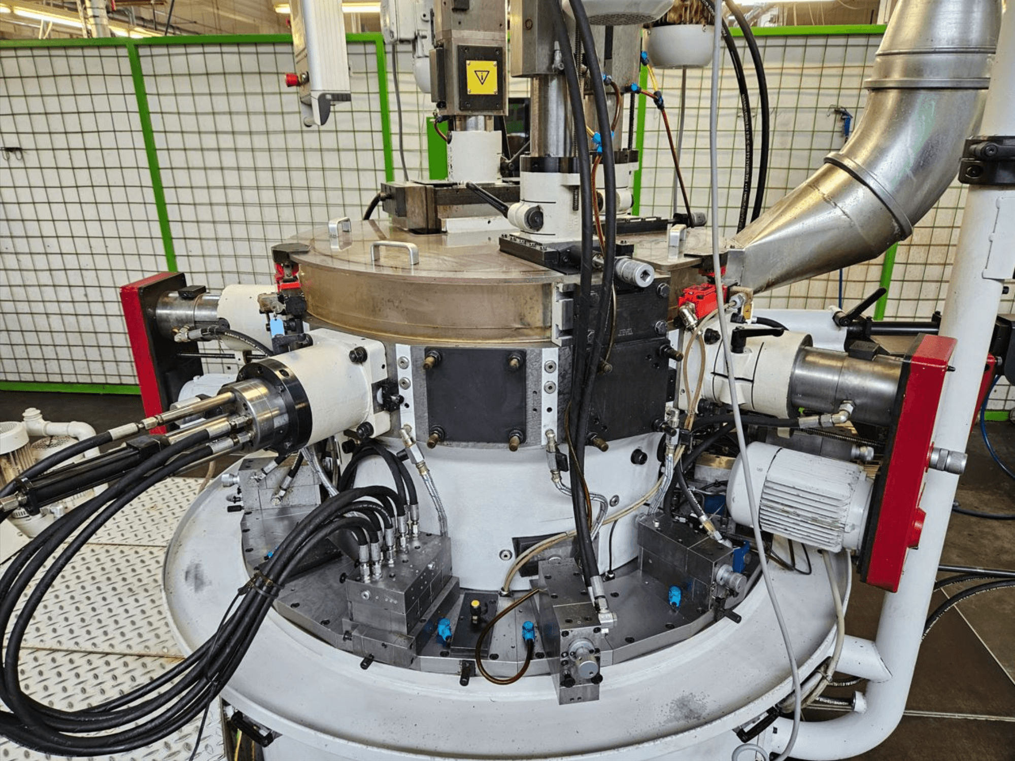 Vista em grande plano de uma máquina industrial com mangueiras hidráulicas, componentes metálicos e uma base rotativa. Não é visível qualquer marca.