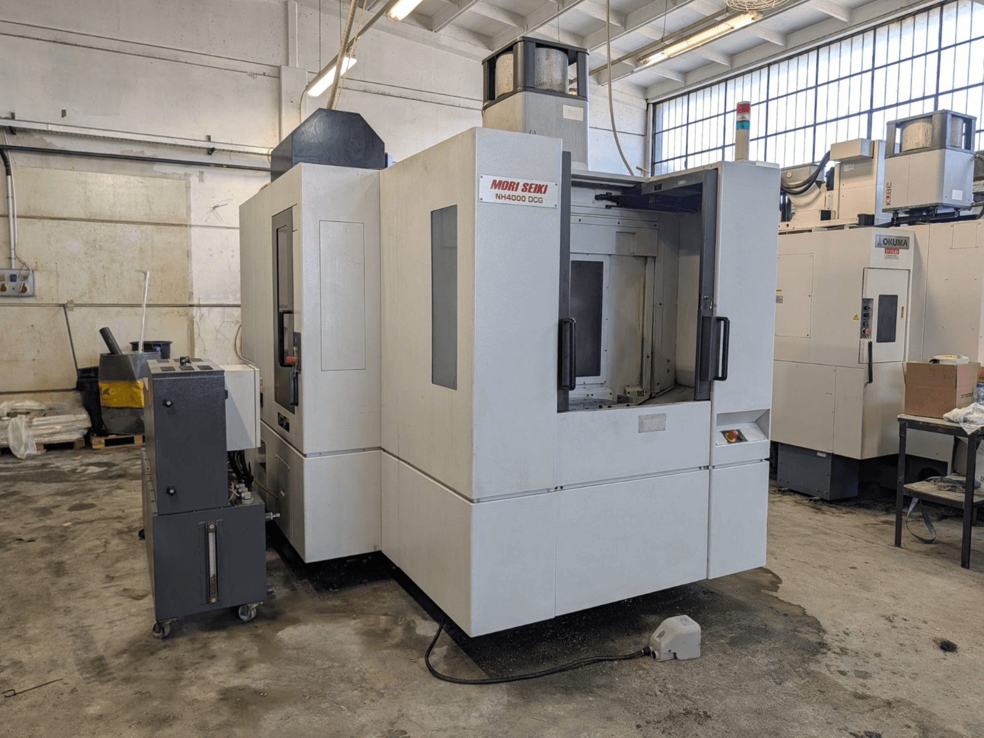 Centro de maquinação horizontal MORI SEIKI NH 4000 DCG, vista frontal, mostrando o painel de controlo e a área de trabalho, acabamento cinzento e branco.