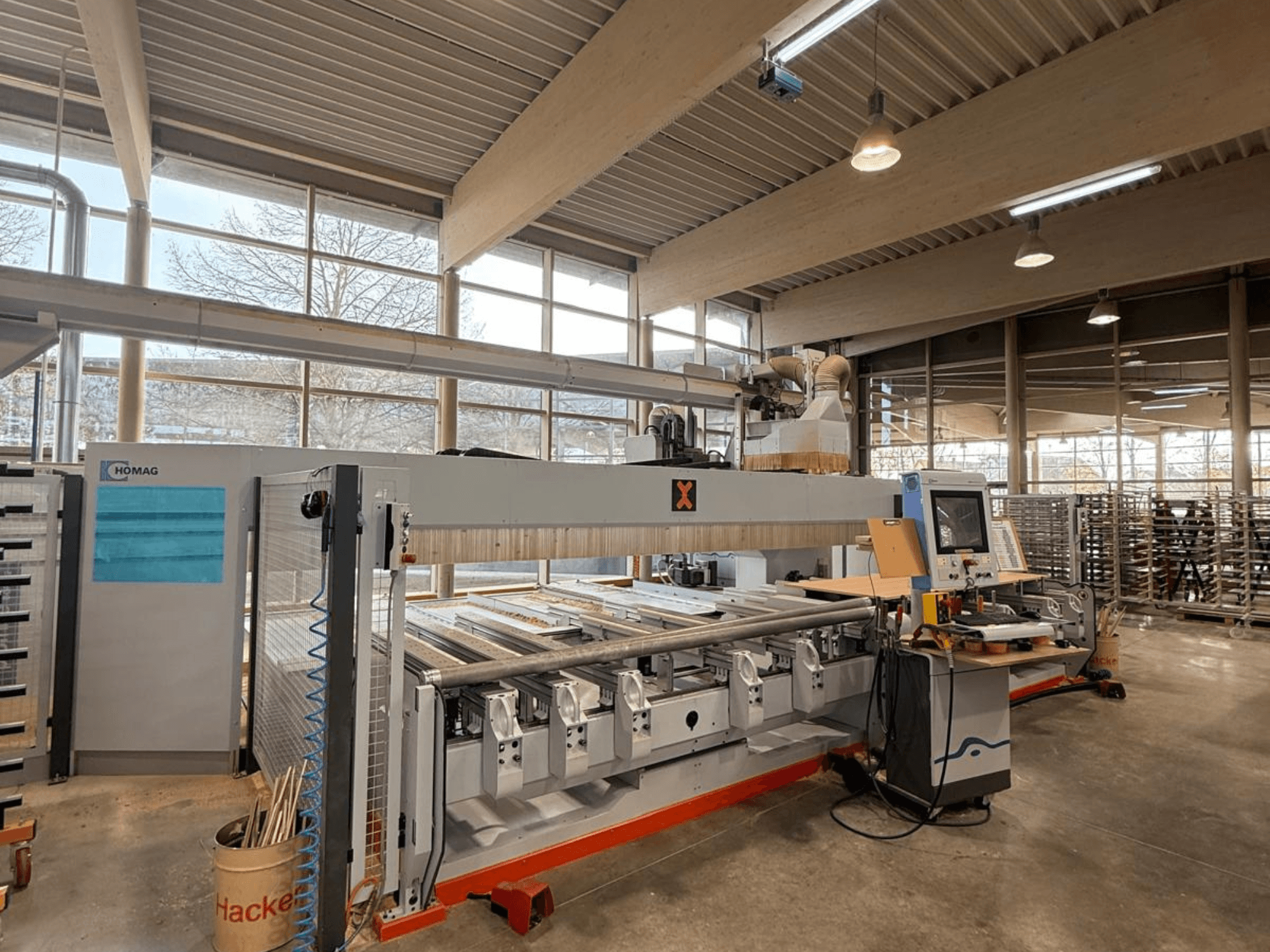 Máquina CNC HOMAG numa oficina, vista frontal, apresentando um painel de controlo e várias ranhuras para ferramentas para trabalhos de precisão em madeira.