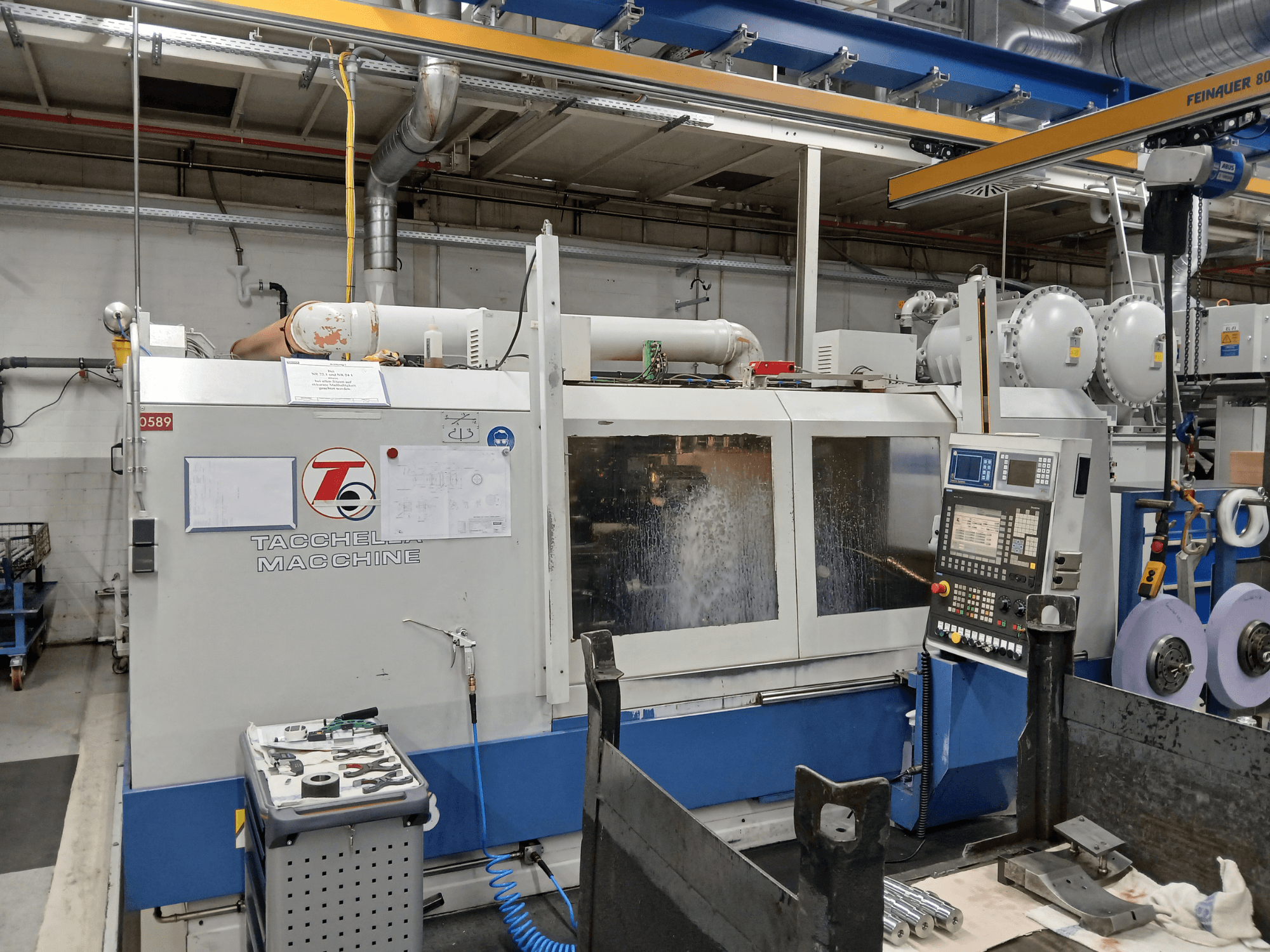 Centro de maquinação Tacchella em vista frontal, com painel de controlo e ferramentas visíveis. A água de refrigeração é pulverizada durante o funcionamento.