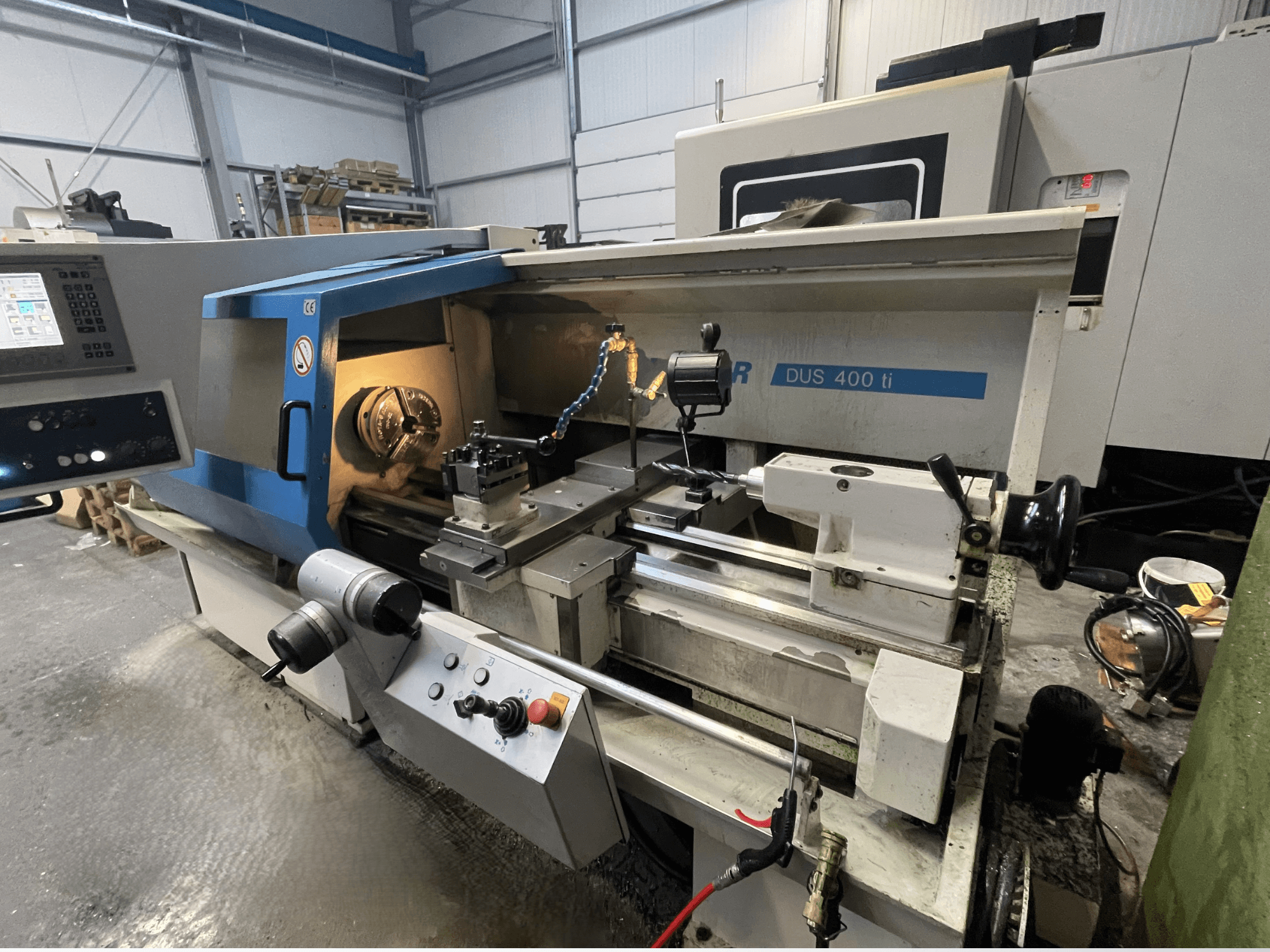 Torno CNC DUS 400 ti em vista frontal, com painel de controlo, suporte de ferramentas e área de trabalho iluminada.