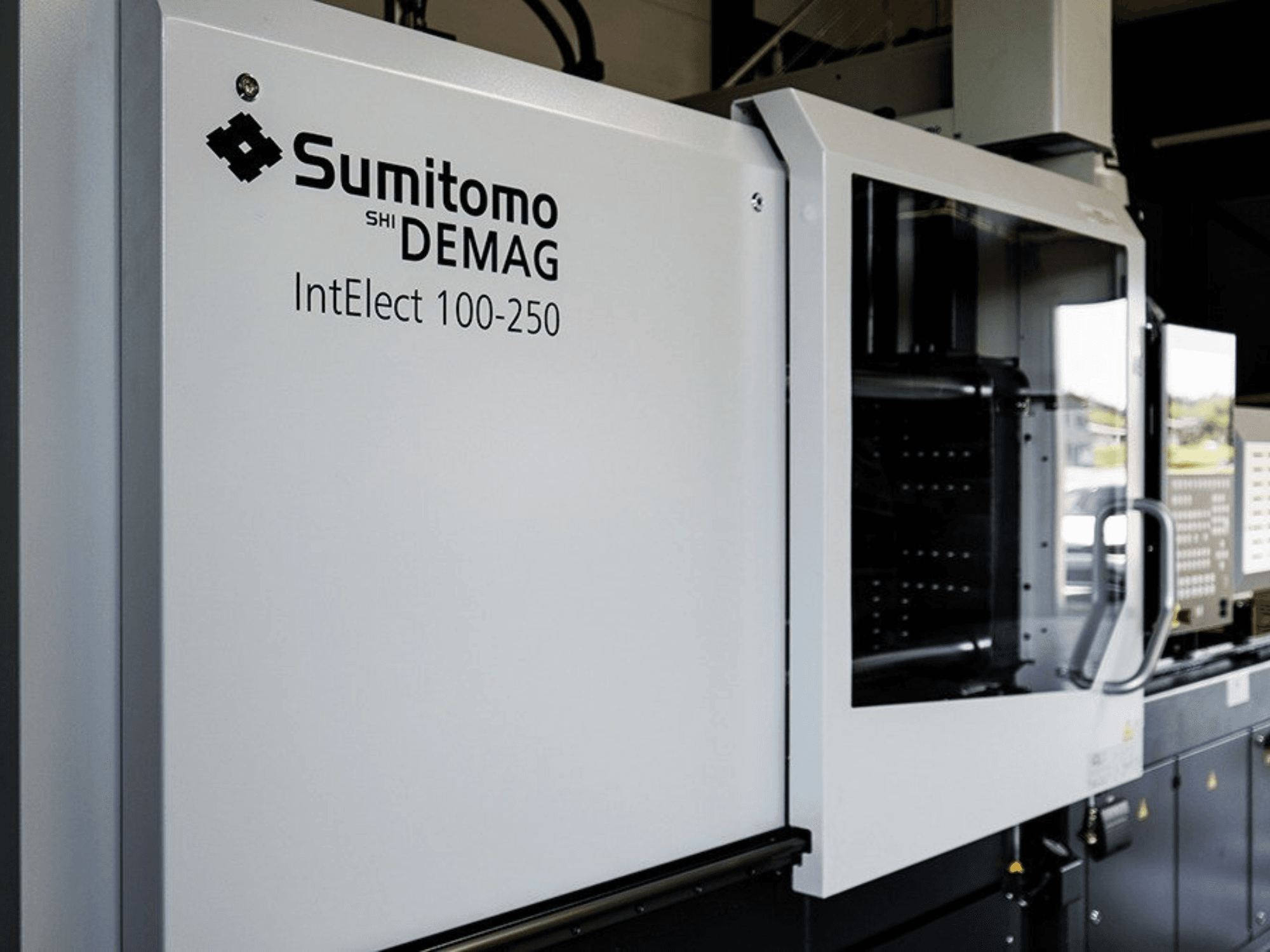 Vista frontal da máquina de moldagem por injeção elétrica SUMITOMO SHI DEMAG IntElect 100/250, com painel de controlo e dispositivos de segurança.