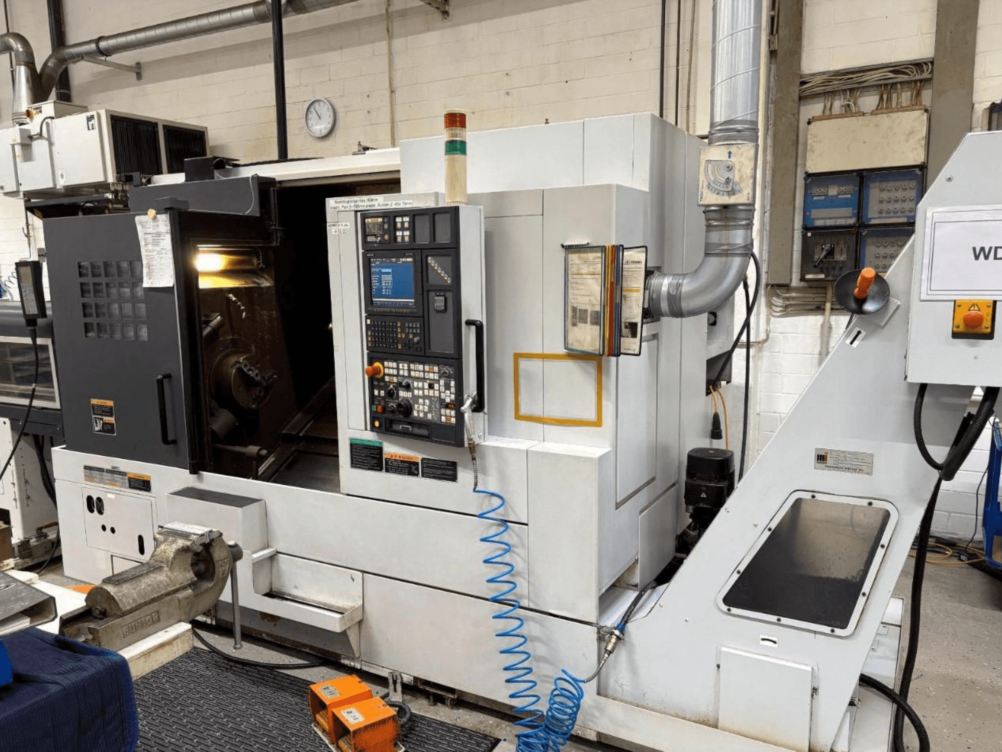 Centro de torneamento-fresagem MORI SEIKI NL 2500 SY, vista frontal, mostrando o painel de controlo e a área de maquinação. Sistema de refrigeração e acessórios visíveis.