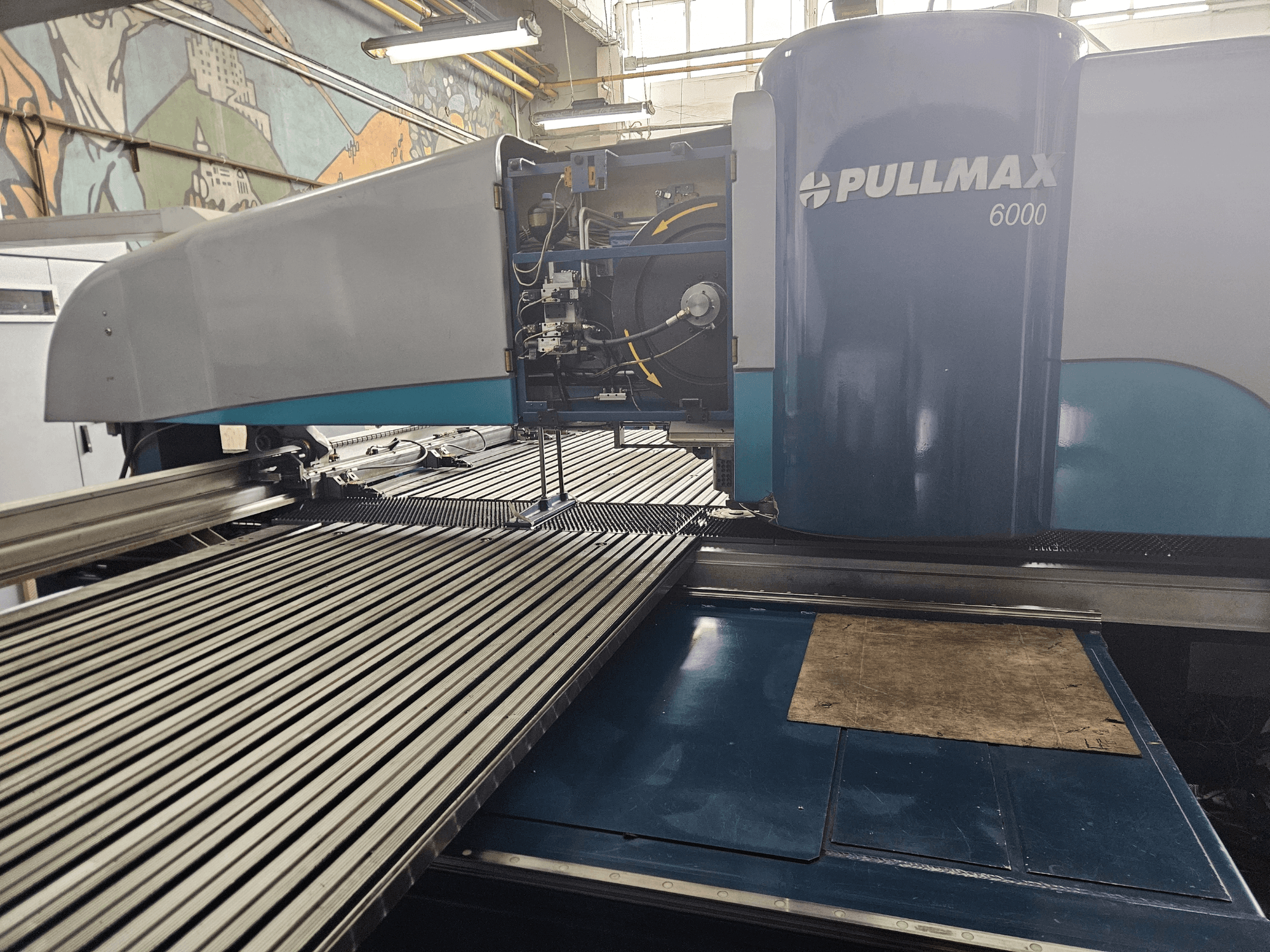 Vista frontal de uma máquina de perfuração CNC Pullmax 6000, com um design elegante, painel operacional e superfície de trabalho em metal.