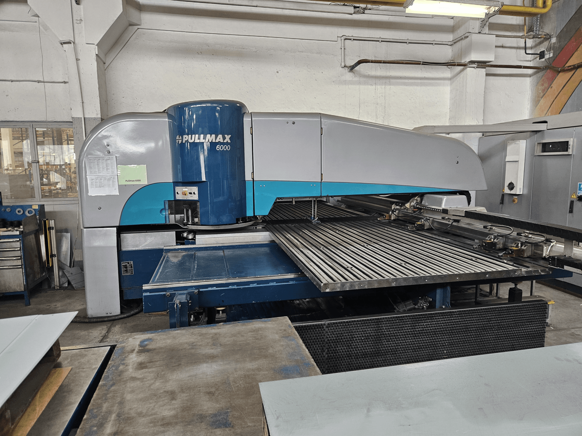 Vista frontal da Puncionadora CNC Pullmax 6000, mostrando a sua grande mesa plana e a estrutura metálica num ambiente de oficina.
