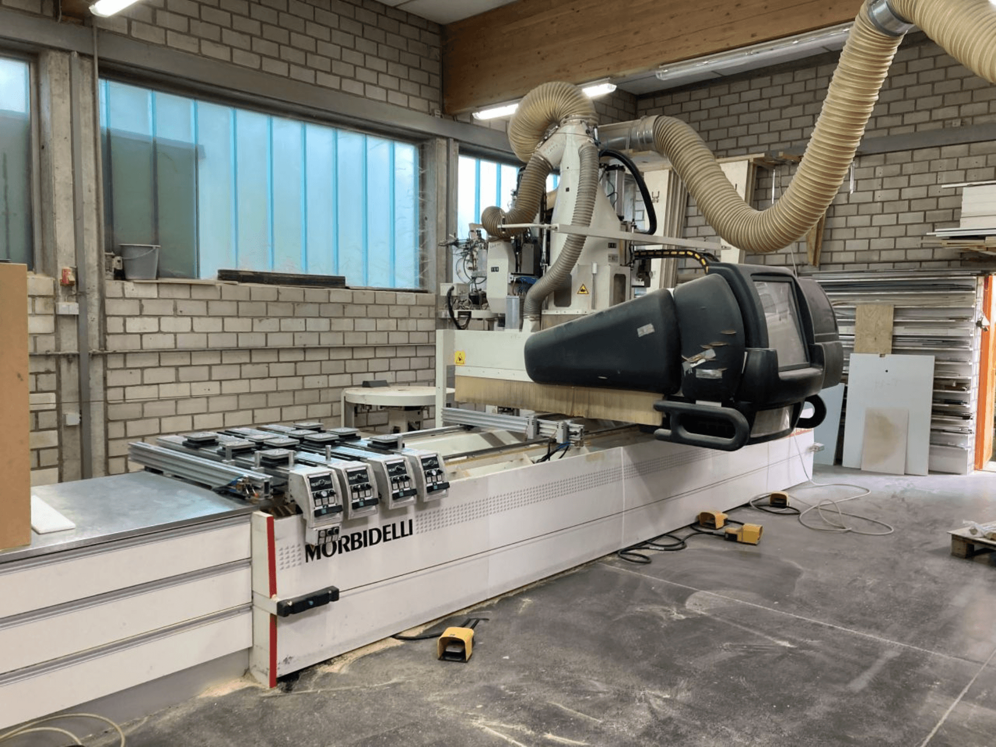 Máquina CNC MORBIDELLI numa oficina, vista frontal com painel de controlo, sistema de extração de poeiras e peça de madeira posicionada.