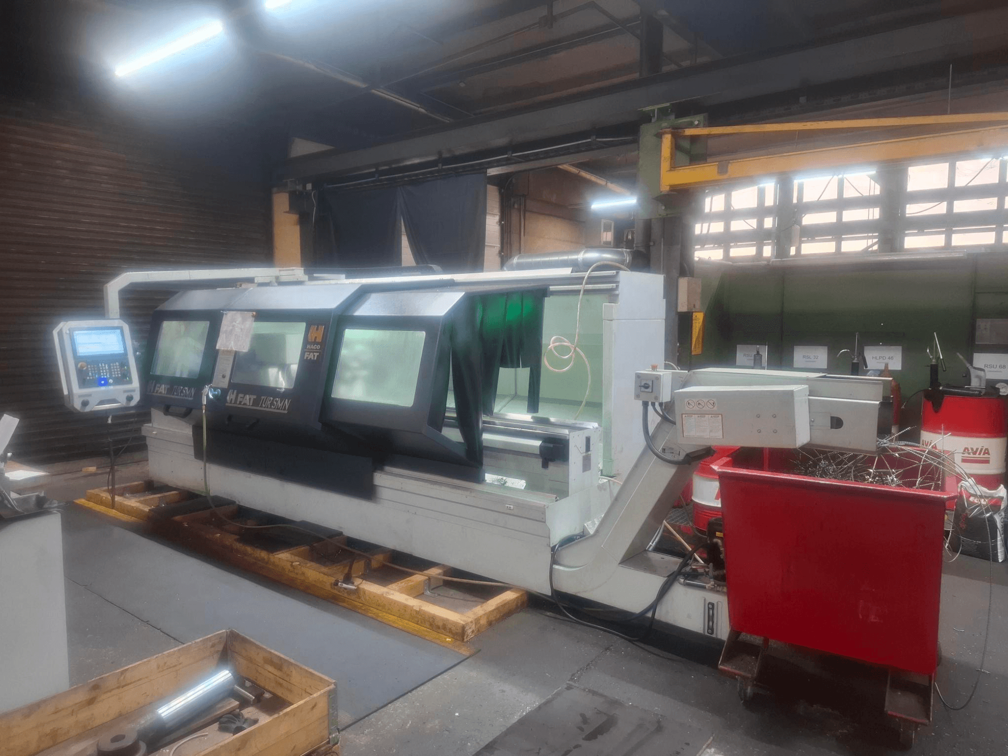 Vista frontal de uma máquina CNC FAT Tursan com painel de controlo, colocada sobre paletes de madeira numa oficina.