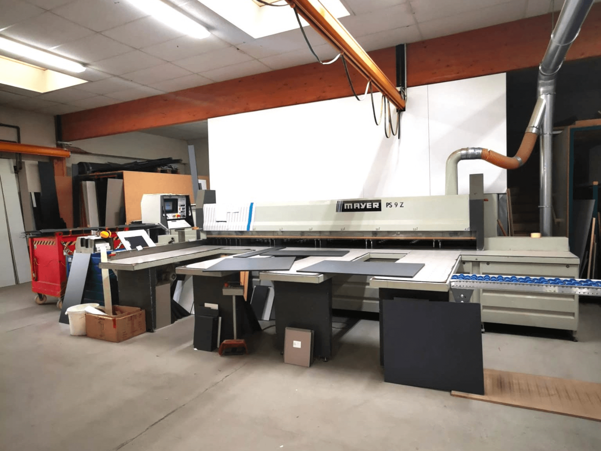 Máquina de corte MAYER PS9 Z numa oficina, vista frontal, com vários materiais e um sistema de transporte visível.