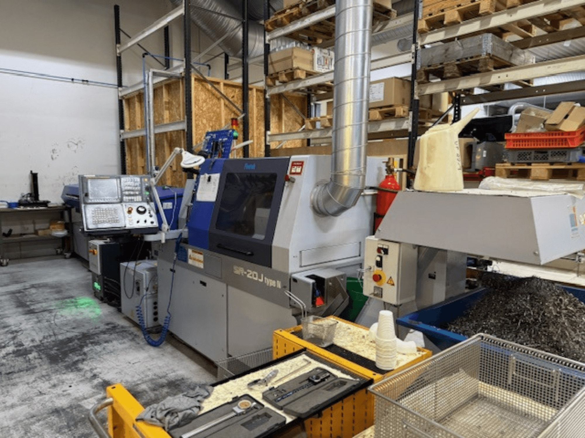 Vista frontal de um centro de maquinação Faroh SPR-20J tipo N com painel de controlo, aparas de metal e equipamento de segurança numa oficina.