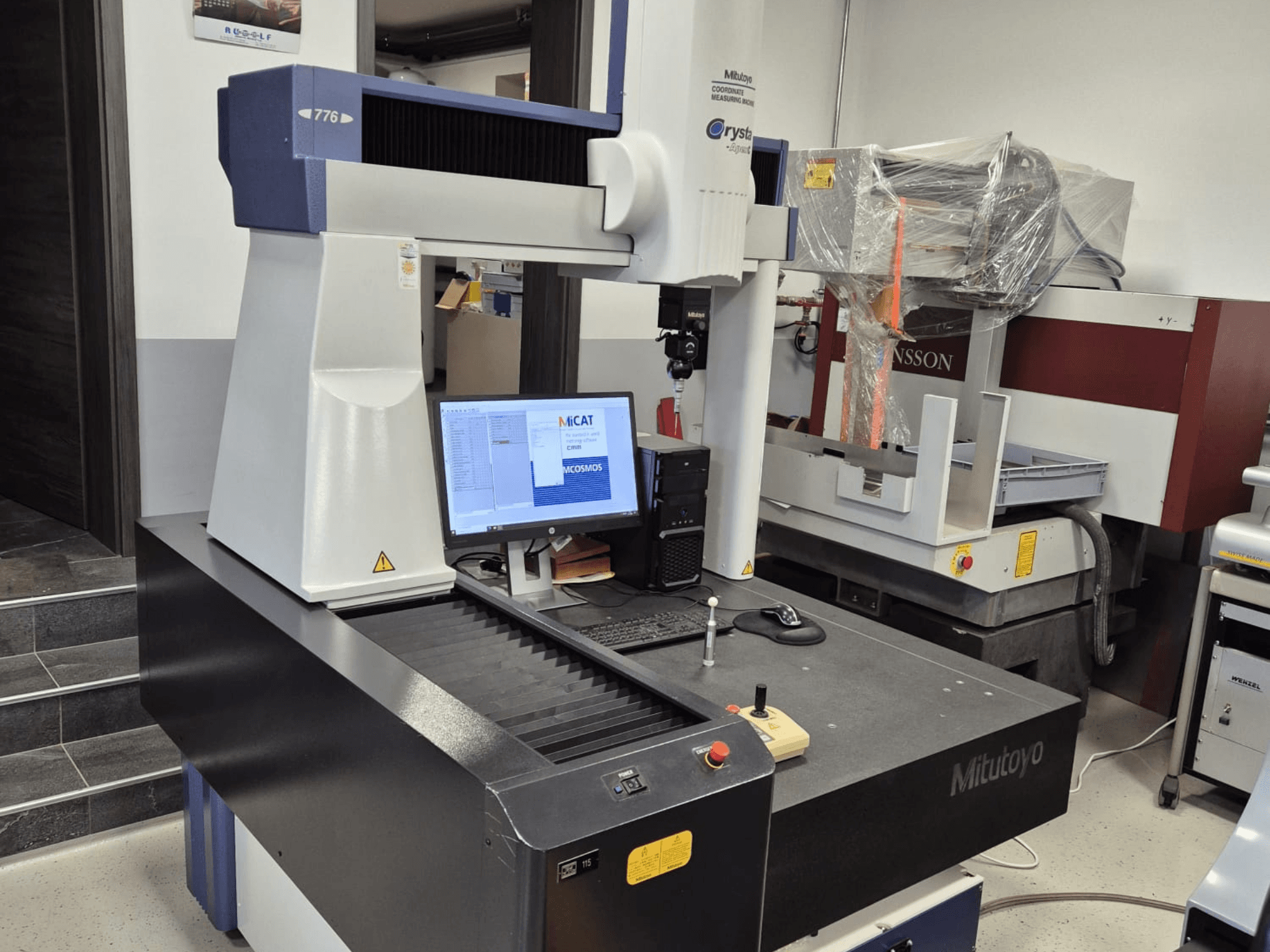 Máquina de medição por coordenadas Mitutoyo modelo 776 em vista frontal, com um monitor que apresenta o software de medição e os controlos visíveis.