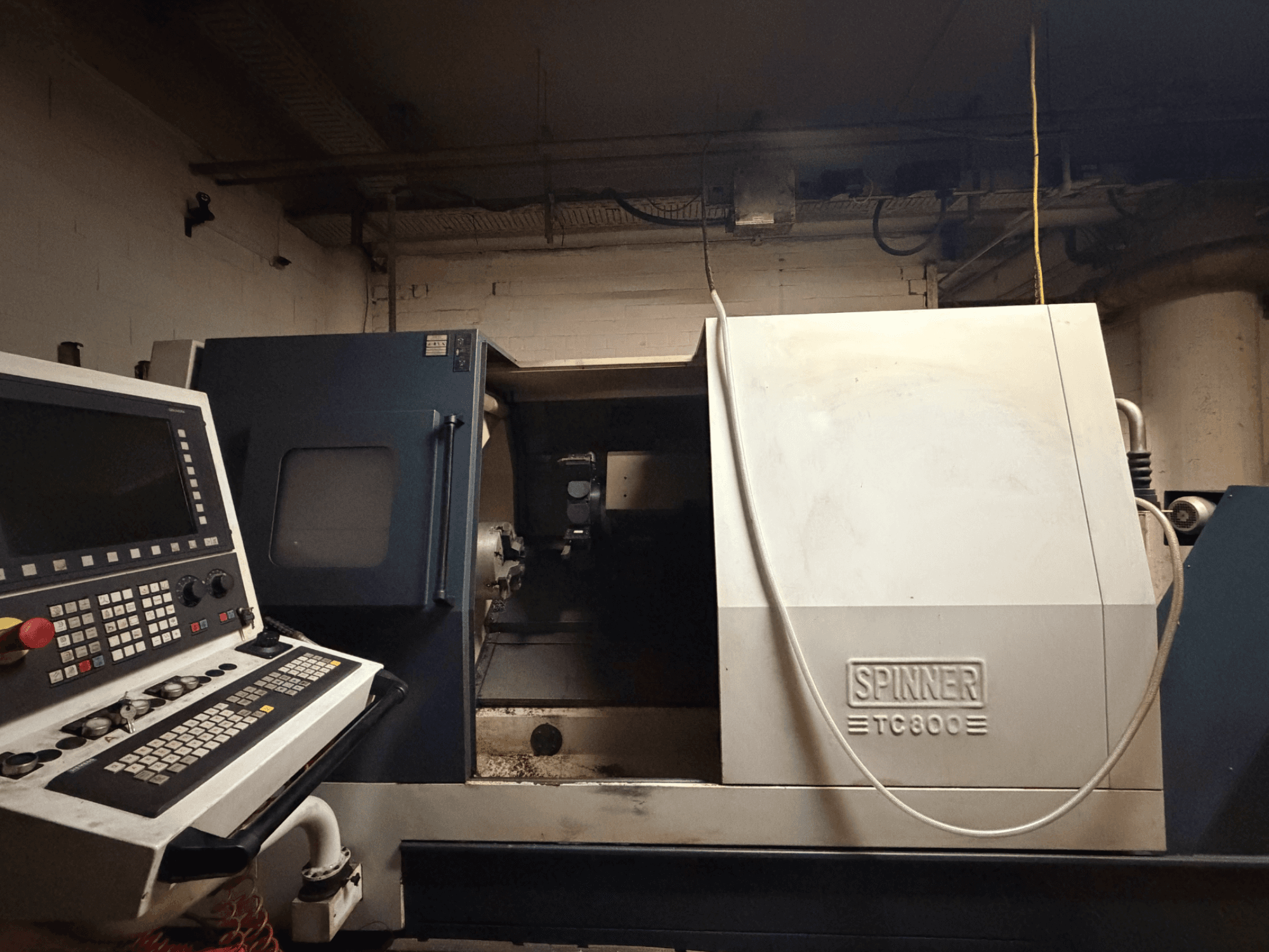 Máquina de tornear horizontal SPINNER TC800, vista frontal com o painel de controlo visível e o interior da máquina ligeiramente exposto.