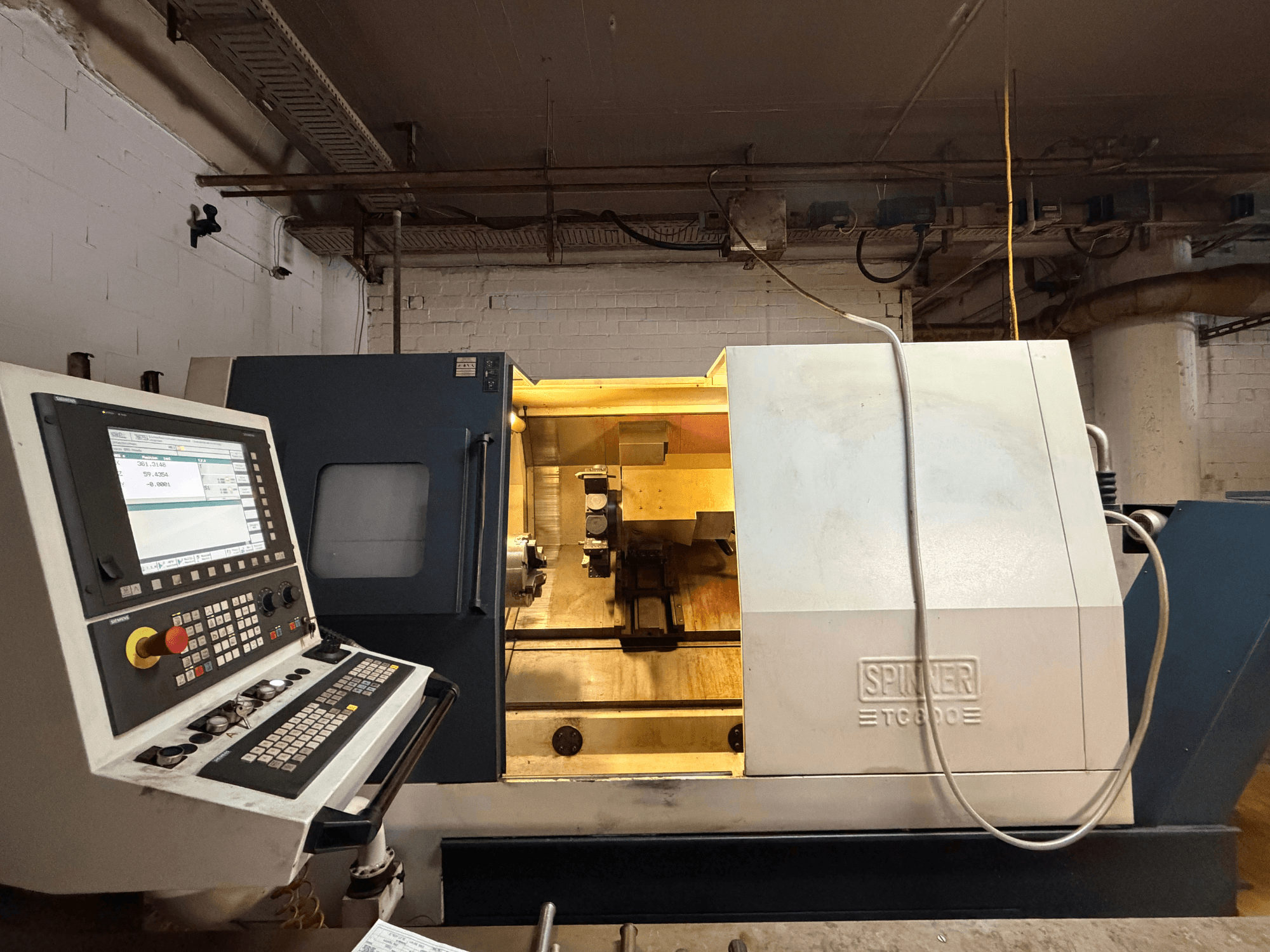Máquina de tornear horizontal SPINNER TC800 numa oficina, com um painel de controlo e componentes internos visíveis.