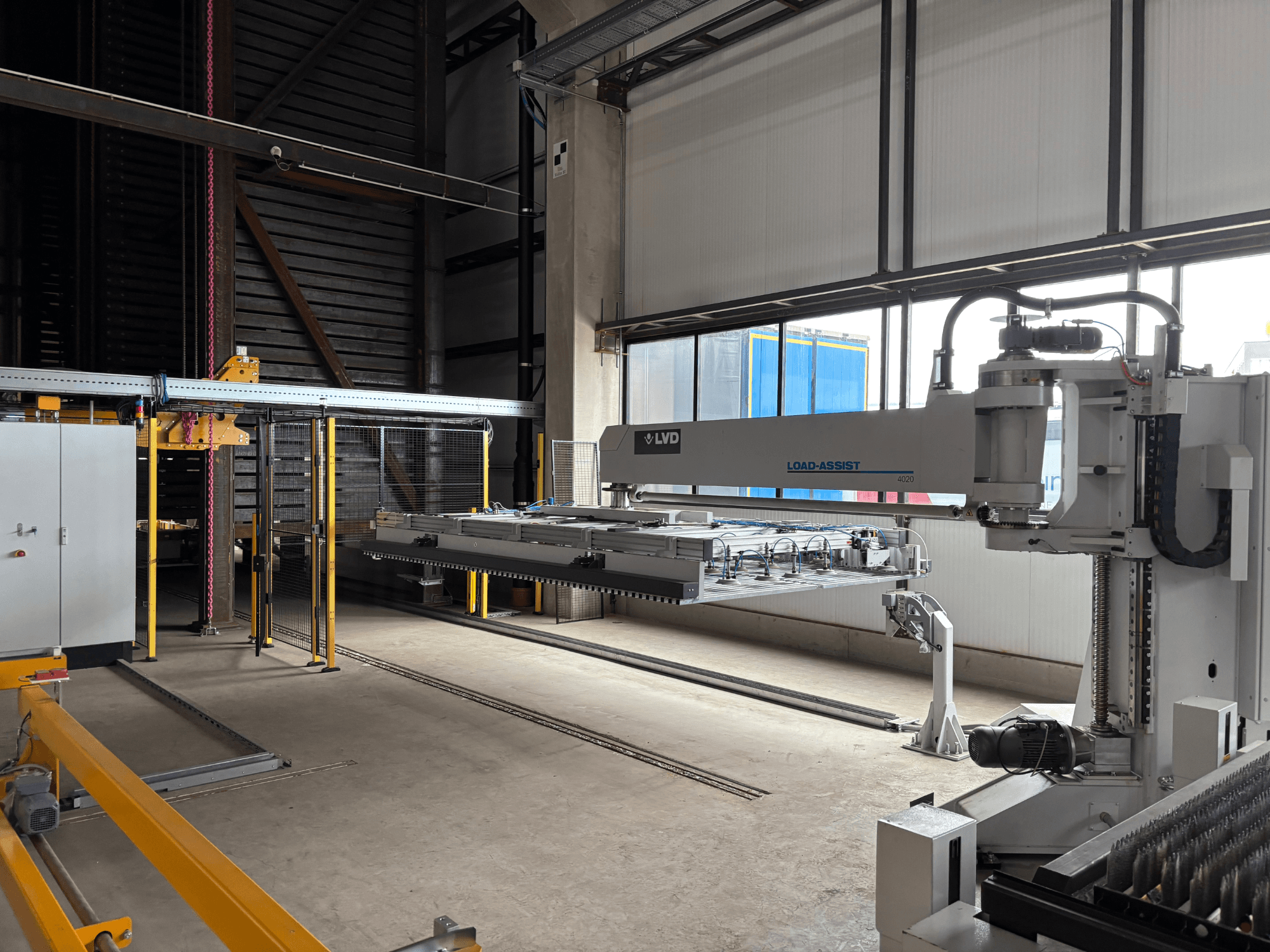 Equipamento de automação LVD Load-Assist 4020 numa vista frontal com um braço robótico e sistema de carregamento visíveis numa grande área de trabalho.