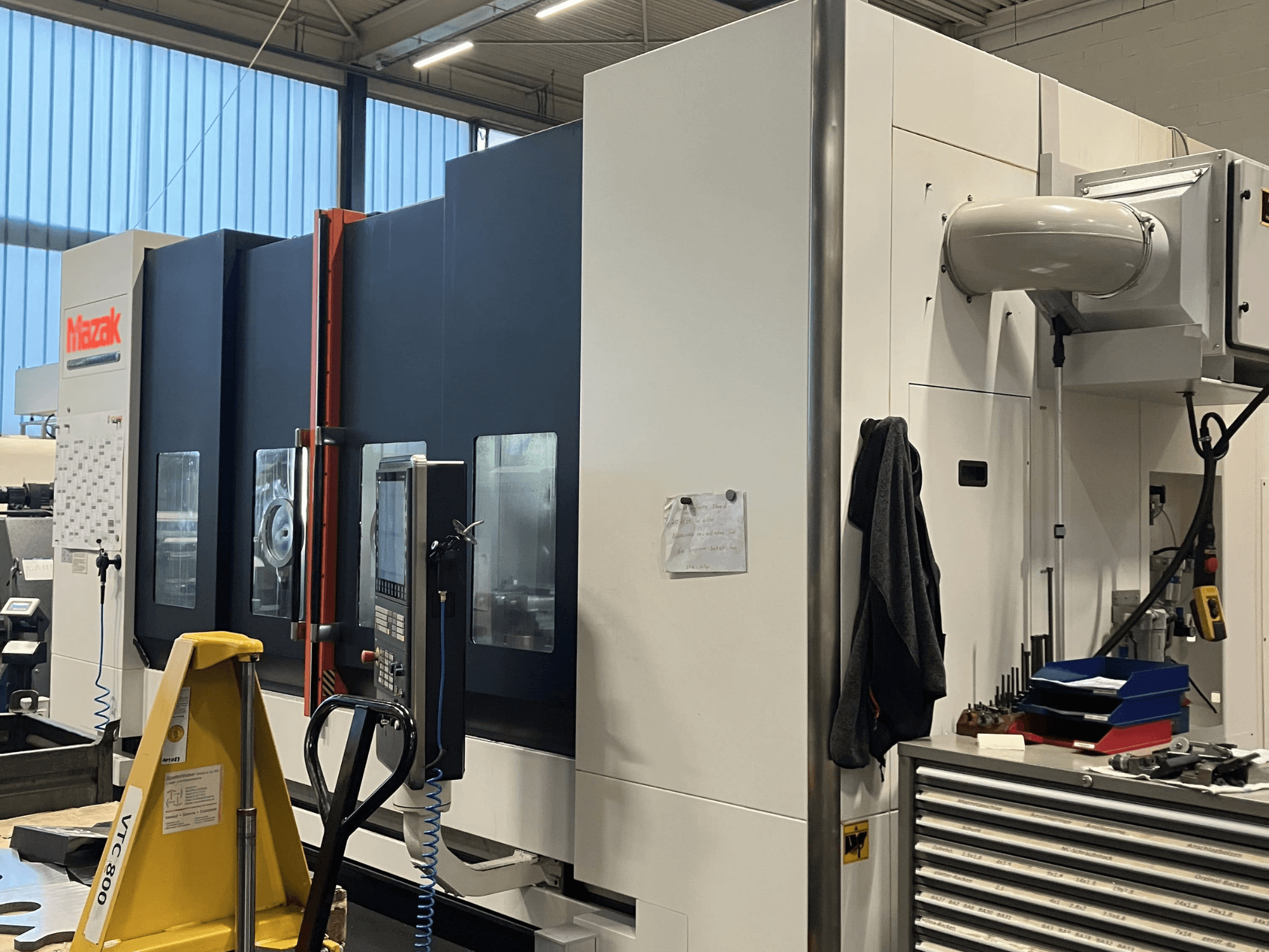 Máquina CNC Mazak vista de lado, mostrando o painel de controlo e as caraterísticas de segurança num ambiente de oficina.