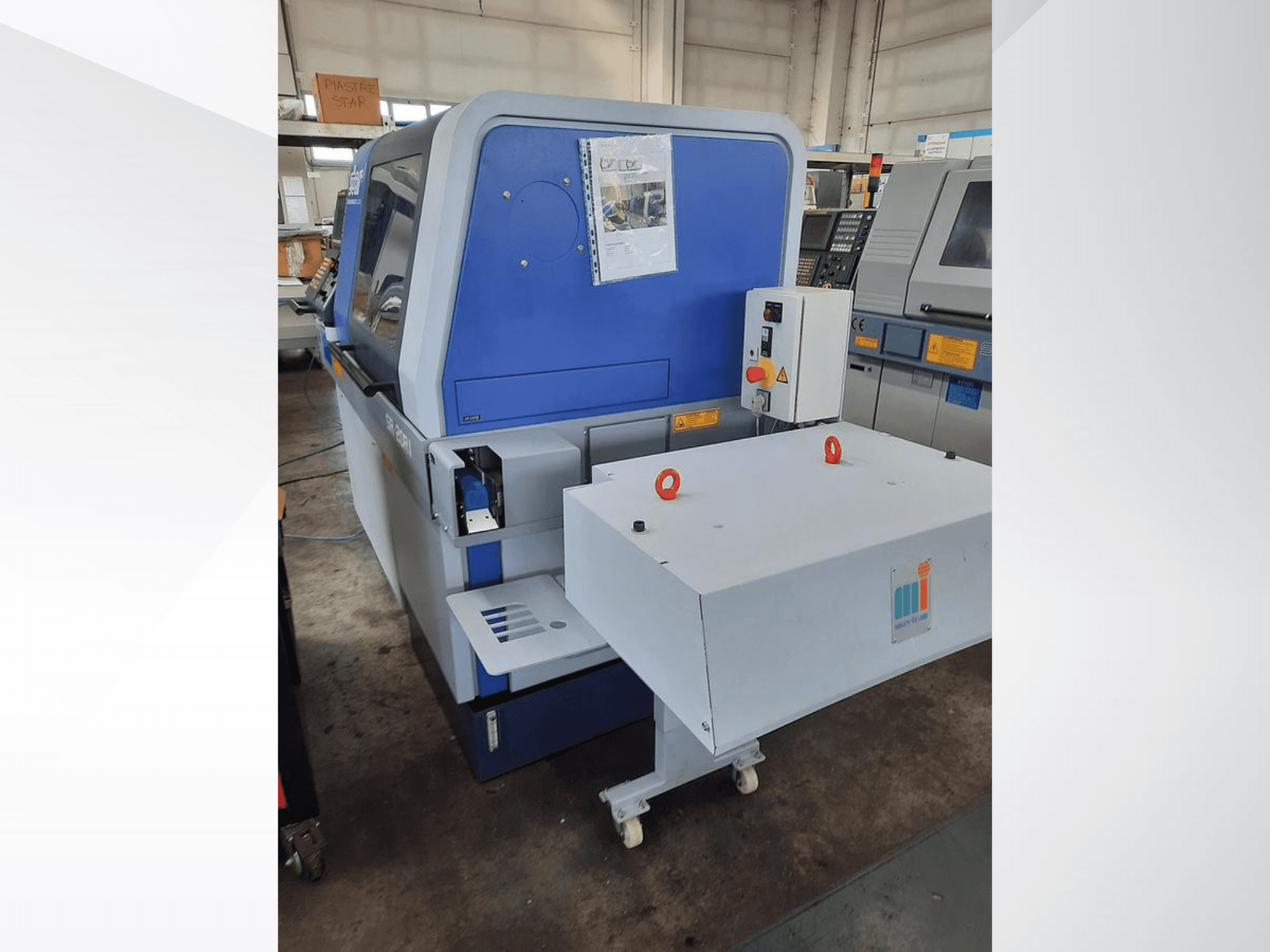 Máquina industrial azul com um tapete rolante branco, mostrando o painel de controlo e os dispositivos de segurança anexados, vista lateral.