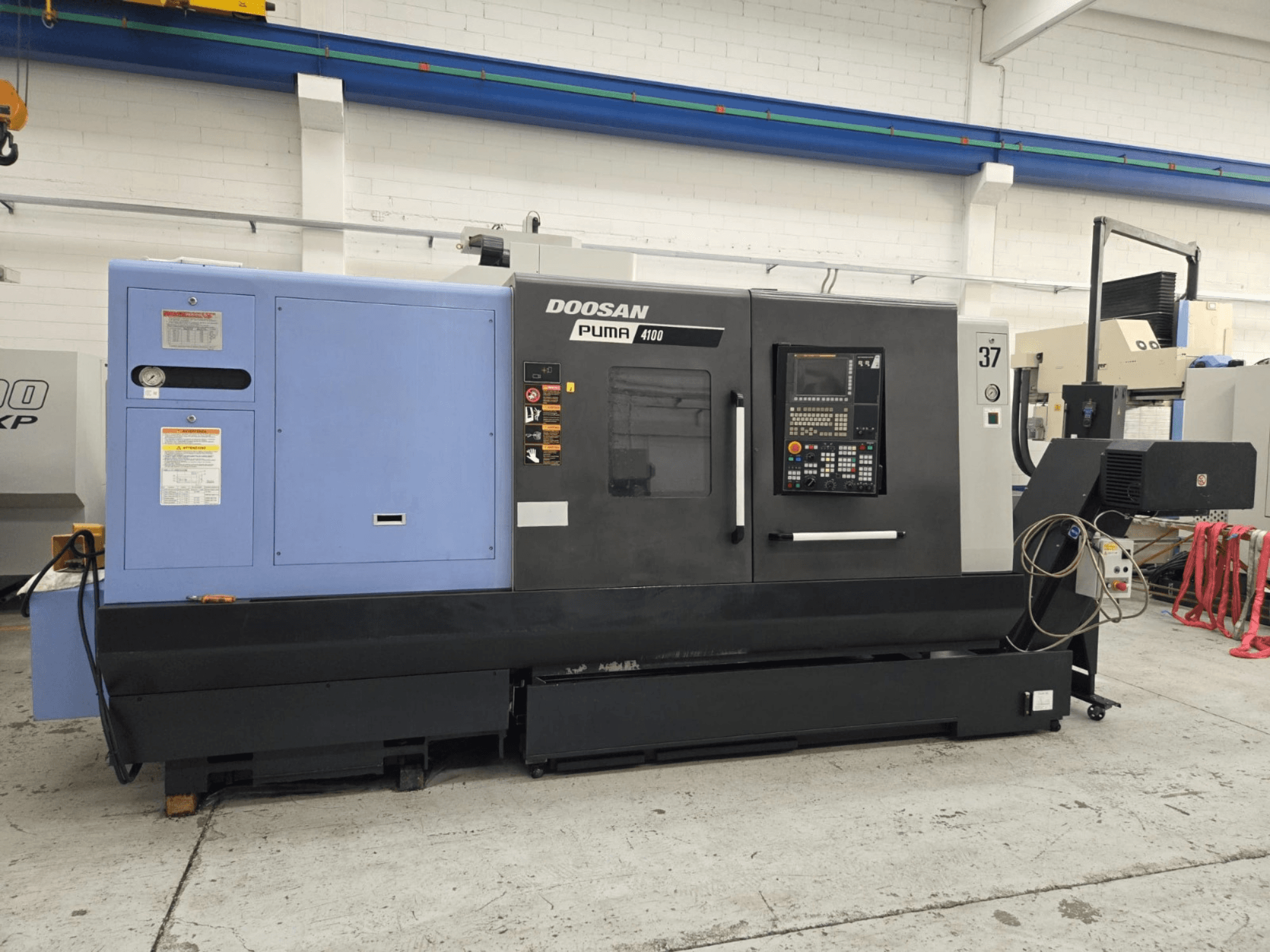 Torno CNC Doosan Puma 4100, vista frontal; possui painel de controlo, unidade de potência azul e etiquetas detalhadas para orientação operacional.