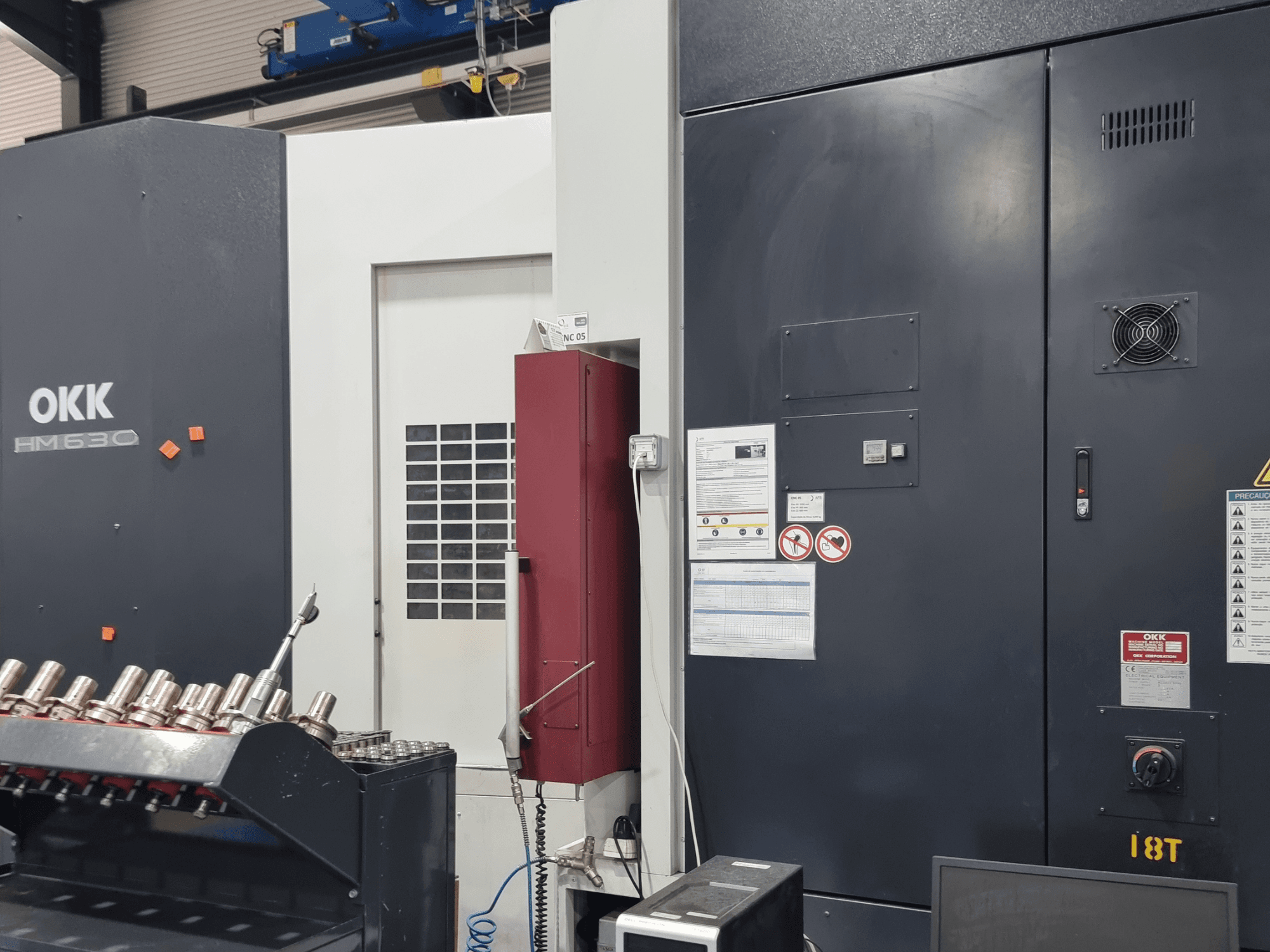 Centro de maquinagem horizontal OKK HM630, vista frontal que mostra o painel de controlo, as instruções de segurança e o compartimento de armazenamento de ferramentas na lateral.