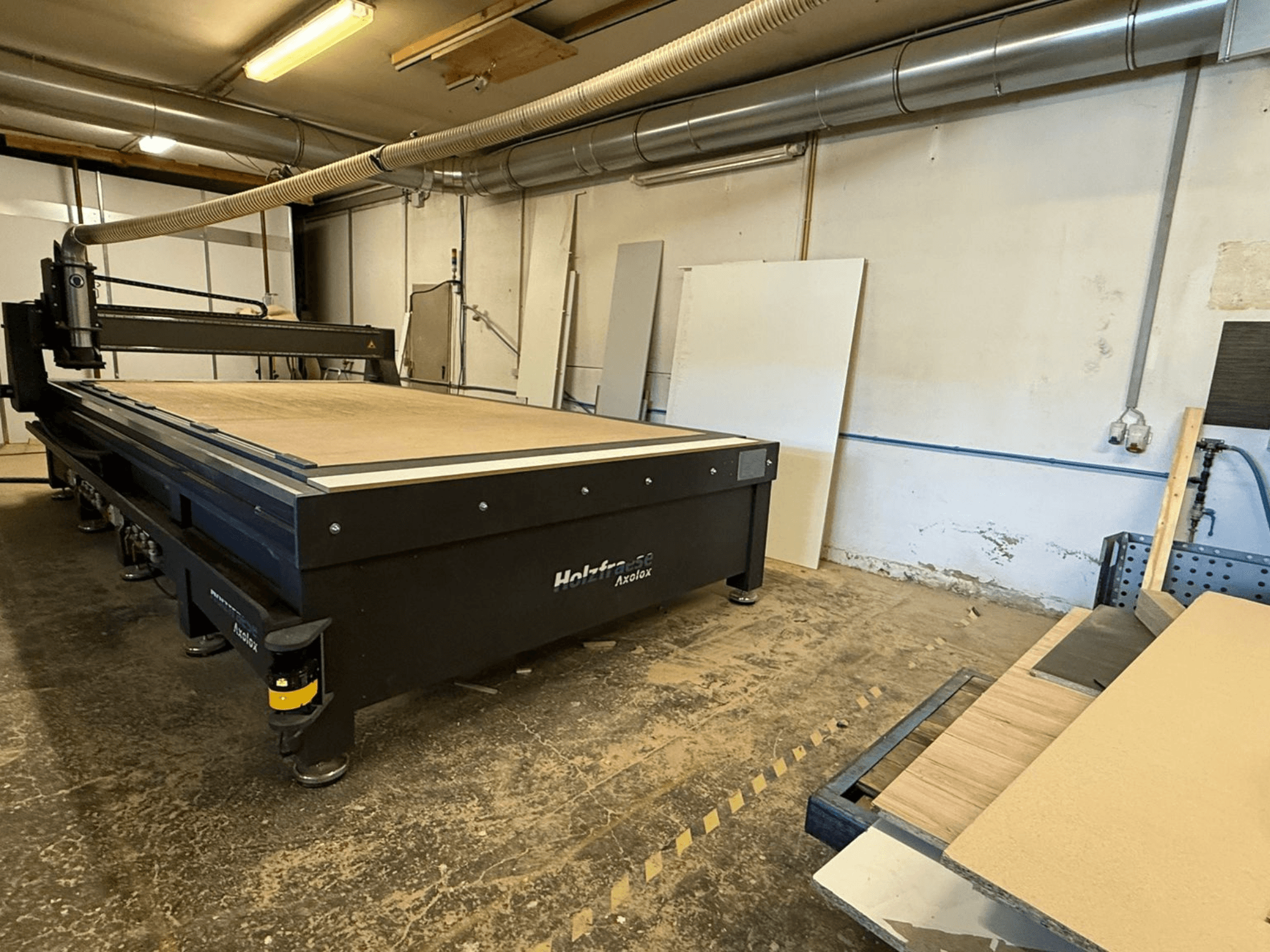Tupia CNC Holz-Her Axos 5 na oficina, vista frontal mostrando a mesa de trabalho, o sistema de extração de poeiras e os painéis de madeira nas proximidades.