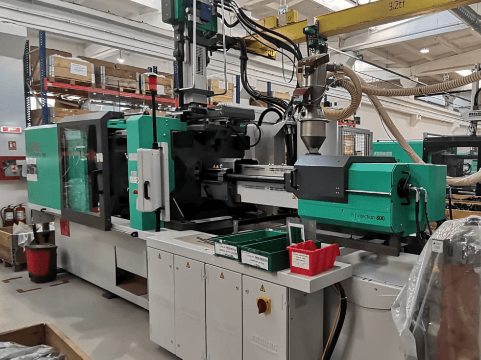 Máquina de injeção H 800 numa fábrica, vista frontal, com um design verde e preto, com painéis de controlo e caixas para peças.