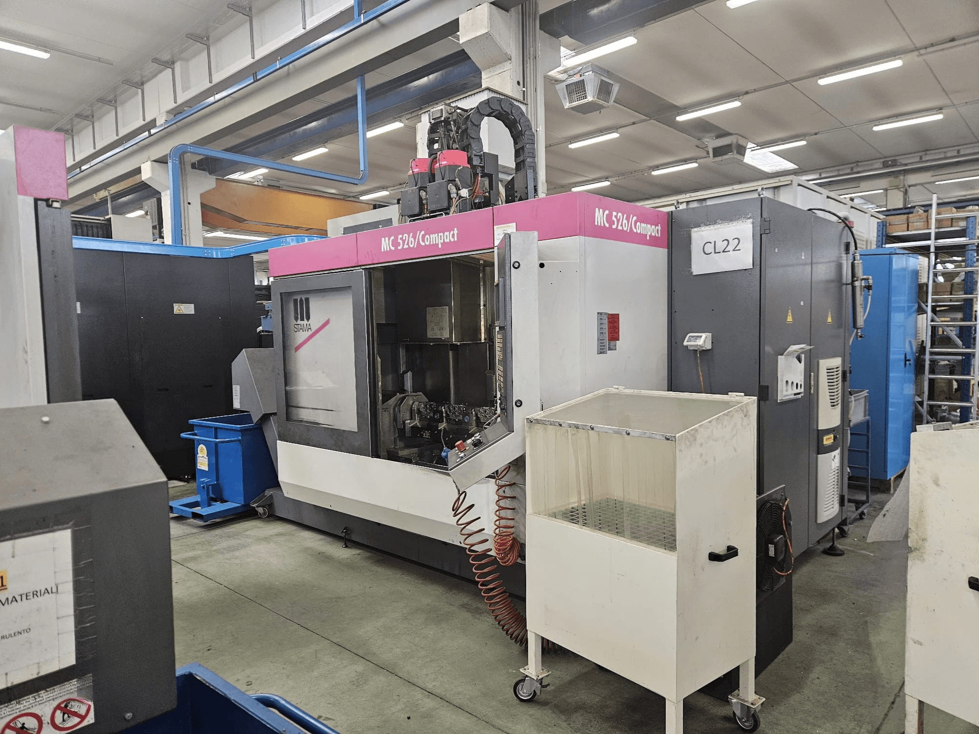 Máquina CNC compacta MC 526 da Stama, vista lateral, mostrando o painel de controlo, o tanque de refrigeração e as máquinas adjacentes.