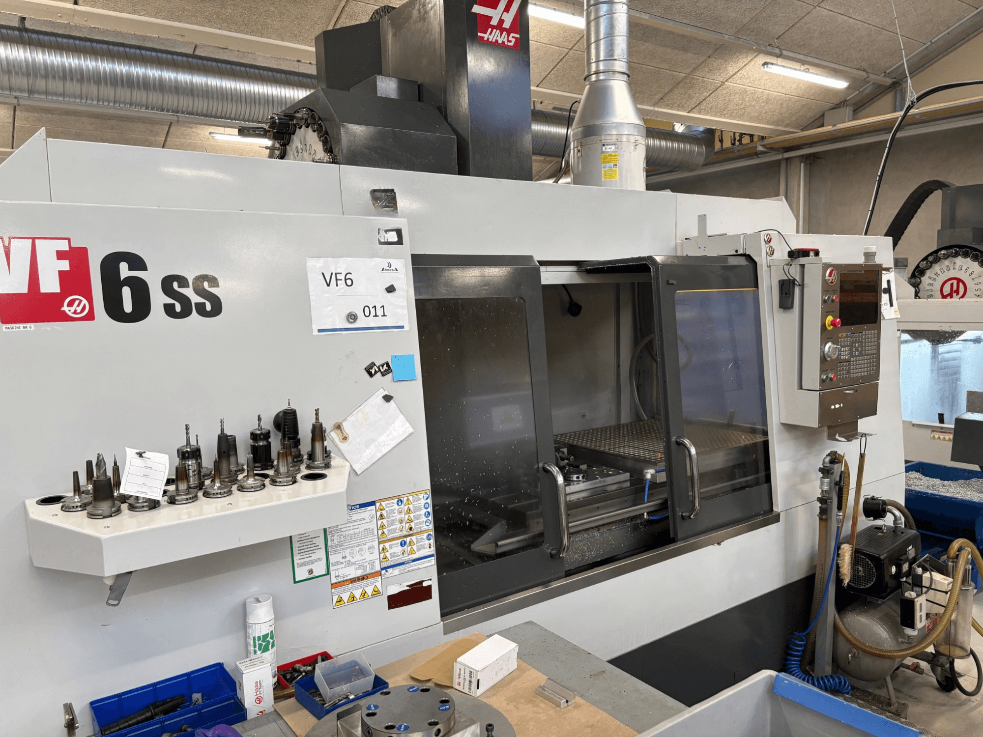 Fresadora CNC Haas VF-6 SS, vista frontal. Apresenta várias ferramentas, painel de controlo e espaço de trabalho interno visível.