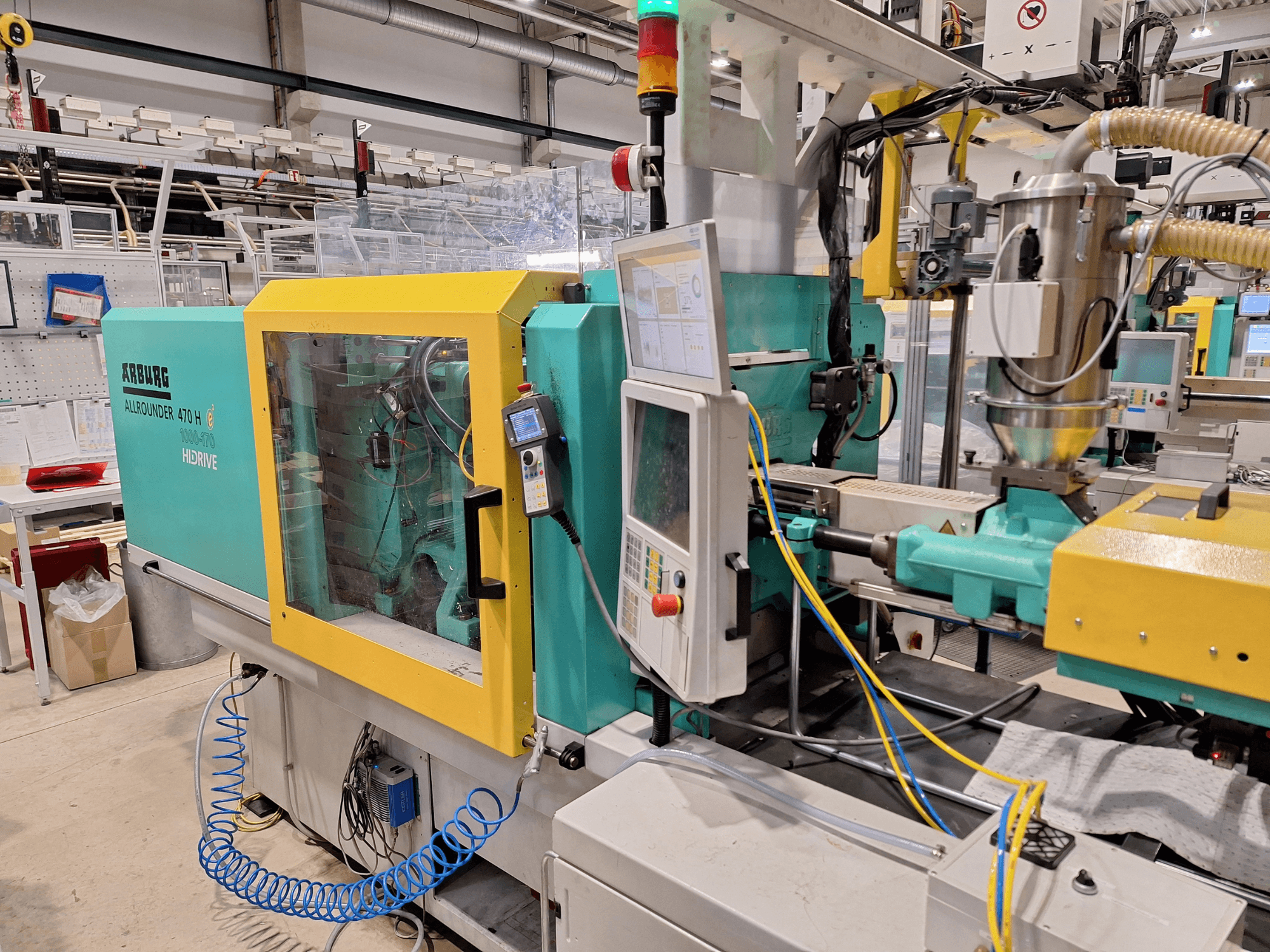 Máquina de moldagem por injeção hidráulica Arburg 470 H 1000-170, vista lateral mostrando o painel de controlo e o sistema de alimentação.