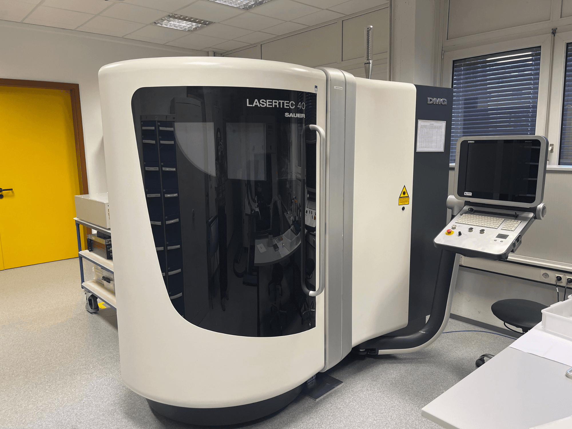 Fresadora LASERTEC 40 branca da DMG MORI, vista de frente, com painel de controlo e design ergonómico numa sala bem iluminada.