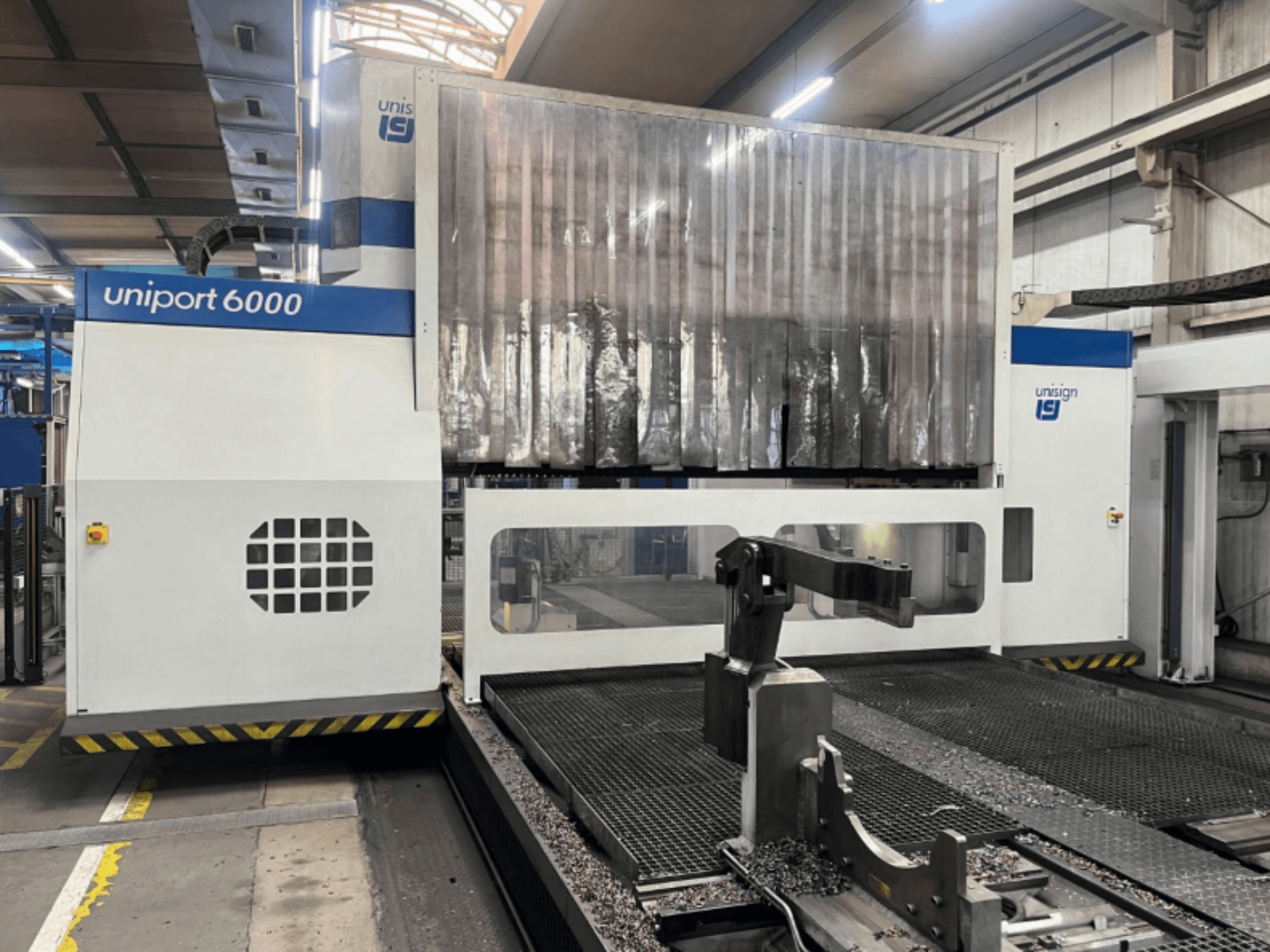 Fresadora de pórtico Unisign uniport 6000, vista frontal, mostrando a estrutura da máquina e a área de corte com aparas de metal.