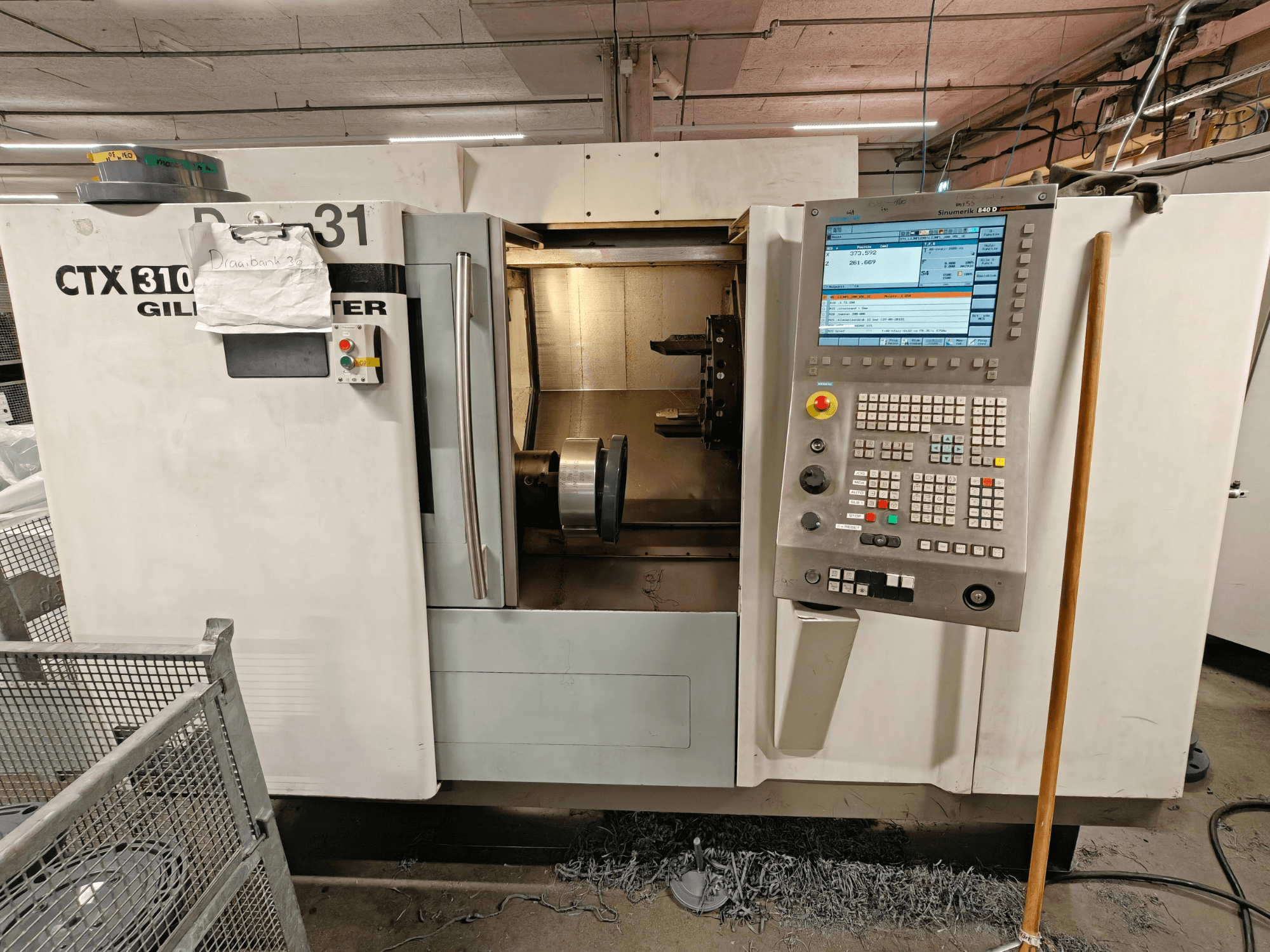 Torneiro horizontal Gildemeister CTX 310, vista frontal com painel de controlo, mostrando ferramentas e espaço de trabalho no interior.